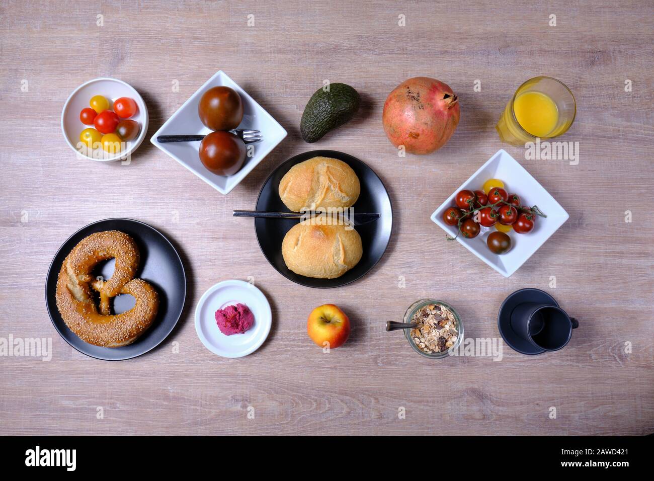 Bretzel, gâteau sucré au thé, marmelade, avocat, tomates, grenade et verre de jus d'orange, disposés symétriquement sur une table en bois sur blanc et Banque D'Images
