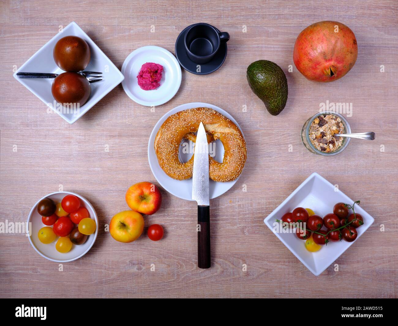 Bretzel, gâteau sucré au thé, marmelade, avocat, tomates, grenade et verre de jus d'orange, disposés symétriquement sur une table en bois sur blanc et Banque D'Images
