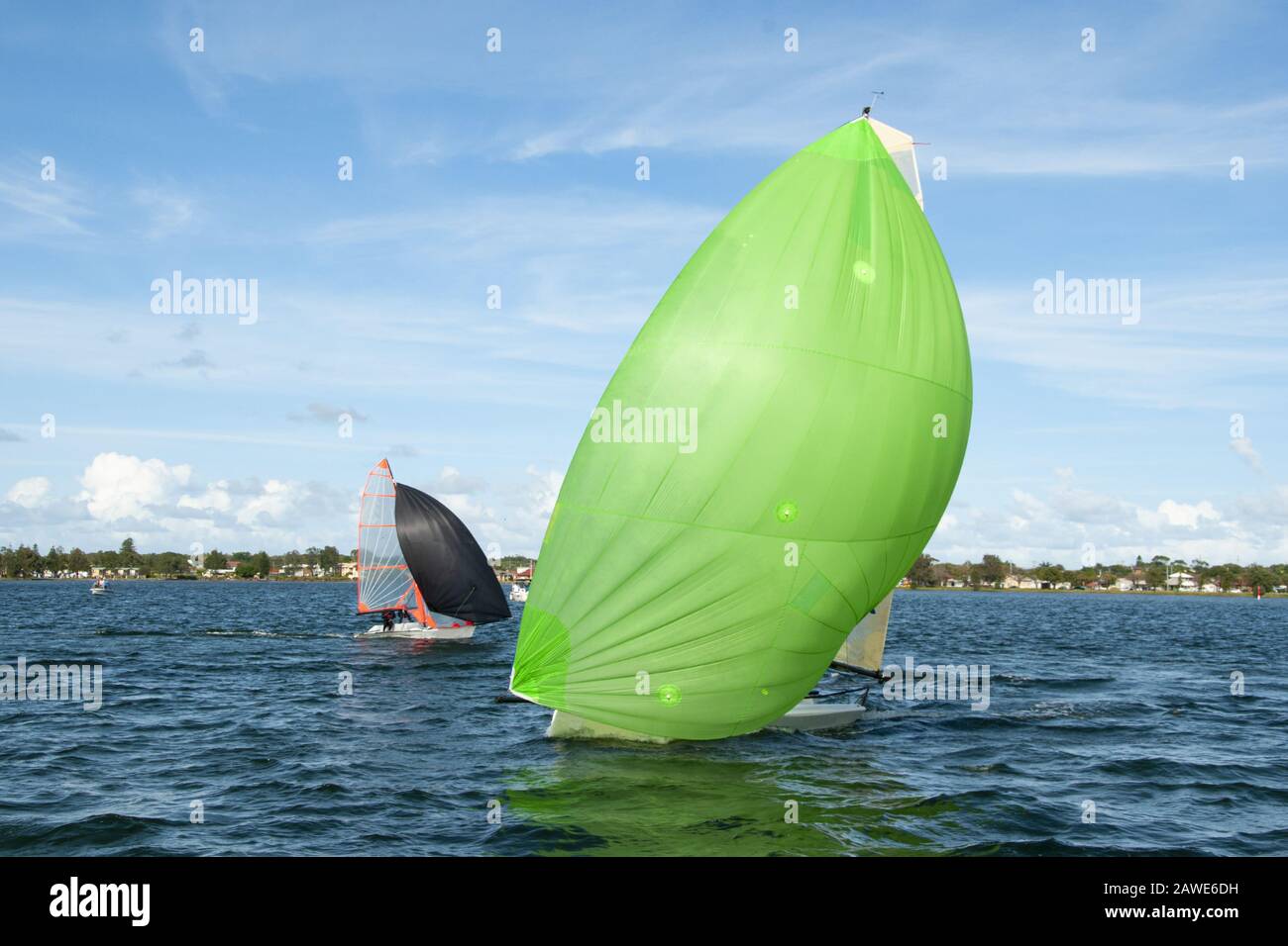 Les enfants naviguant sur un petit voilier se rapprochent avec un spinnaker vert citron entièrement déployé suivi d'un concurrent. Banque D'Images