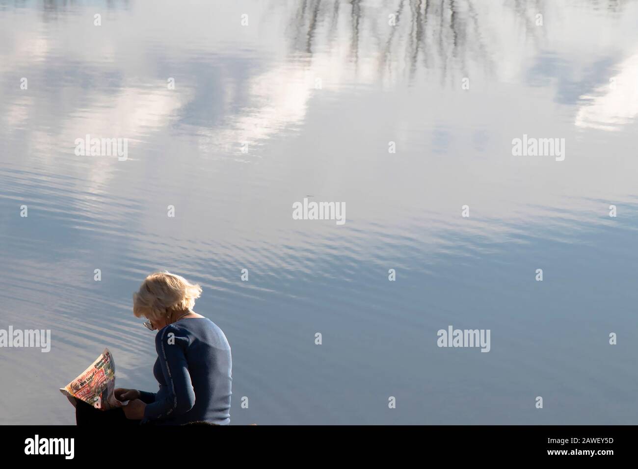 Belgrade, Serbie - 2 février 2020: Une femme âgée assise seule sur une banque de lacs lisant des journaux, avec des réflexions sur l'eau Banque D'Images