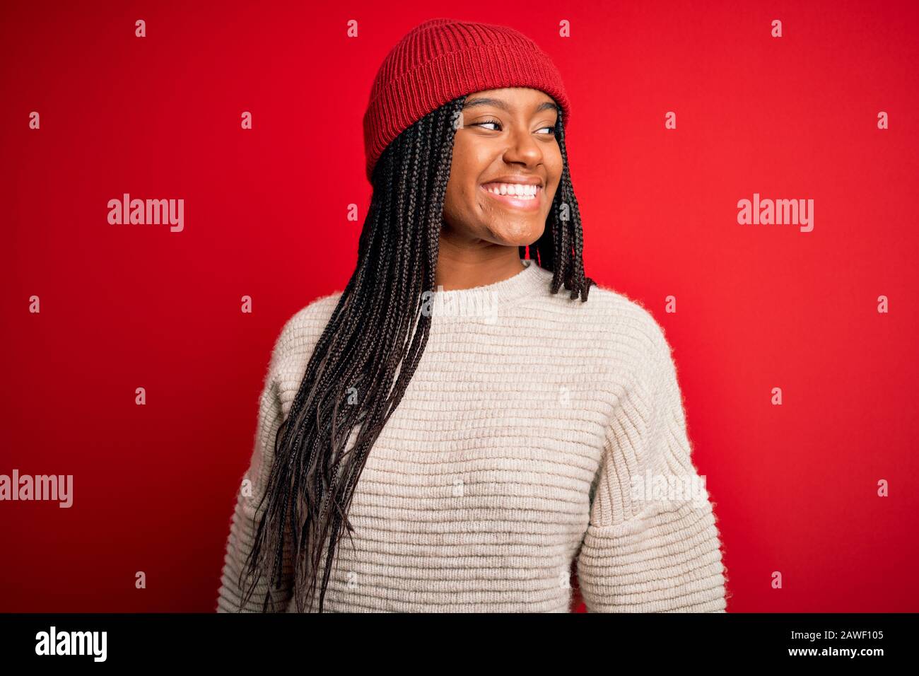 Jeune femme africaine américaine portant un pull d'hiver et un chapeau de  laine sur fond rouge isolé regardant de côté avec sourire sur le visage,  naturel express Photo Stock - Alamy