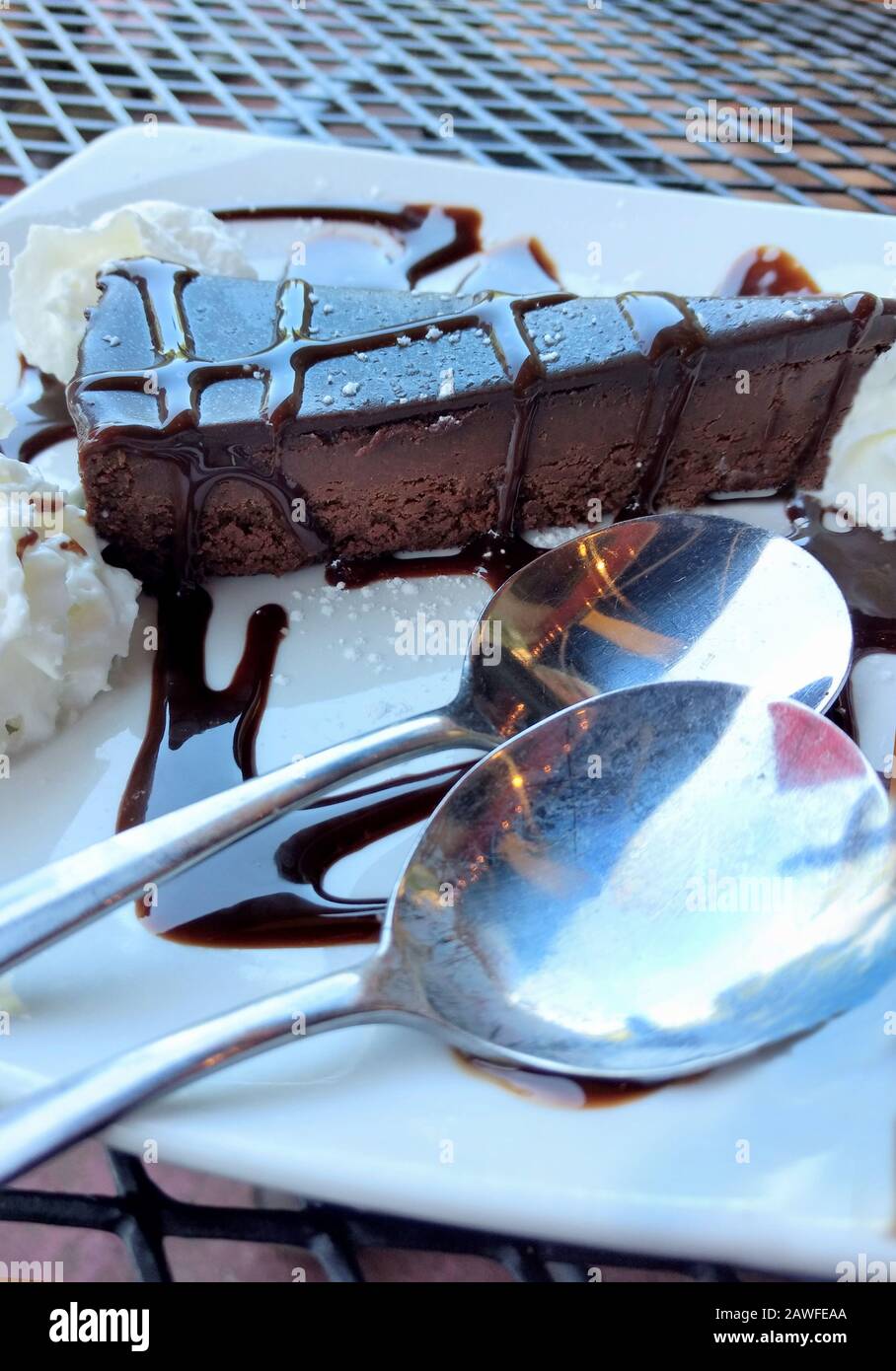 Une tranche crémeuse et décadente de torte au chocolat sans farine est garnie de rubans de sauce au chocolat et servie avec de la crème fouettée et deux cuillères à s Banque D'Images