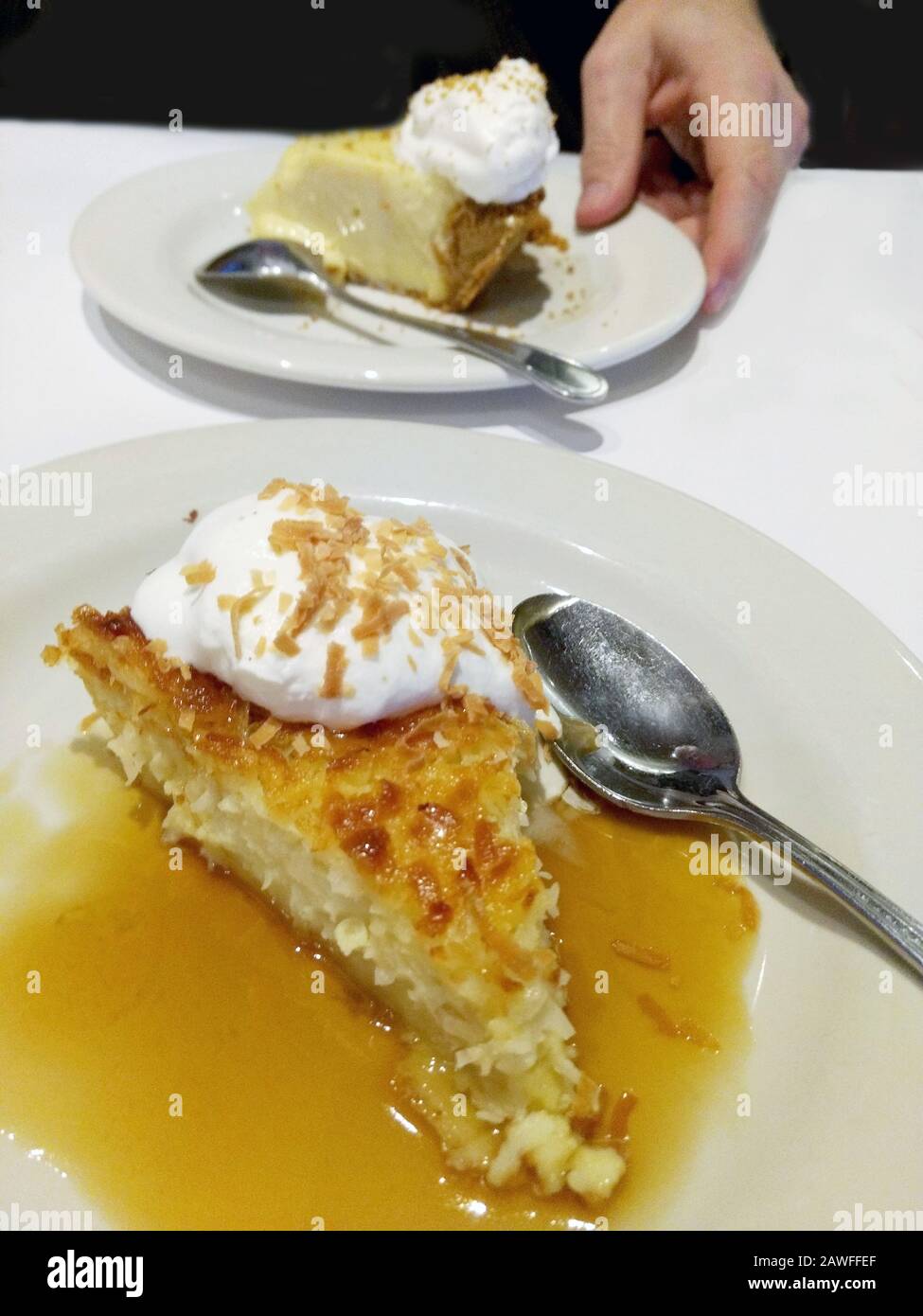 Une tranche de tarte à la crème anglaise de la noix de coco est placée dans un glacer à la vanille bourbon et est surmontée de noix de coco grillées et de crème fouettée. Une main place un morceau de citron vert Banque D'Images
