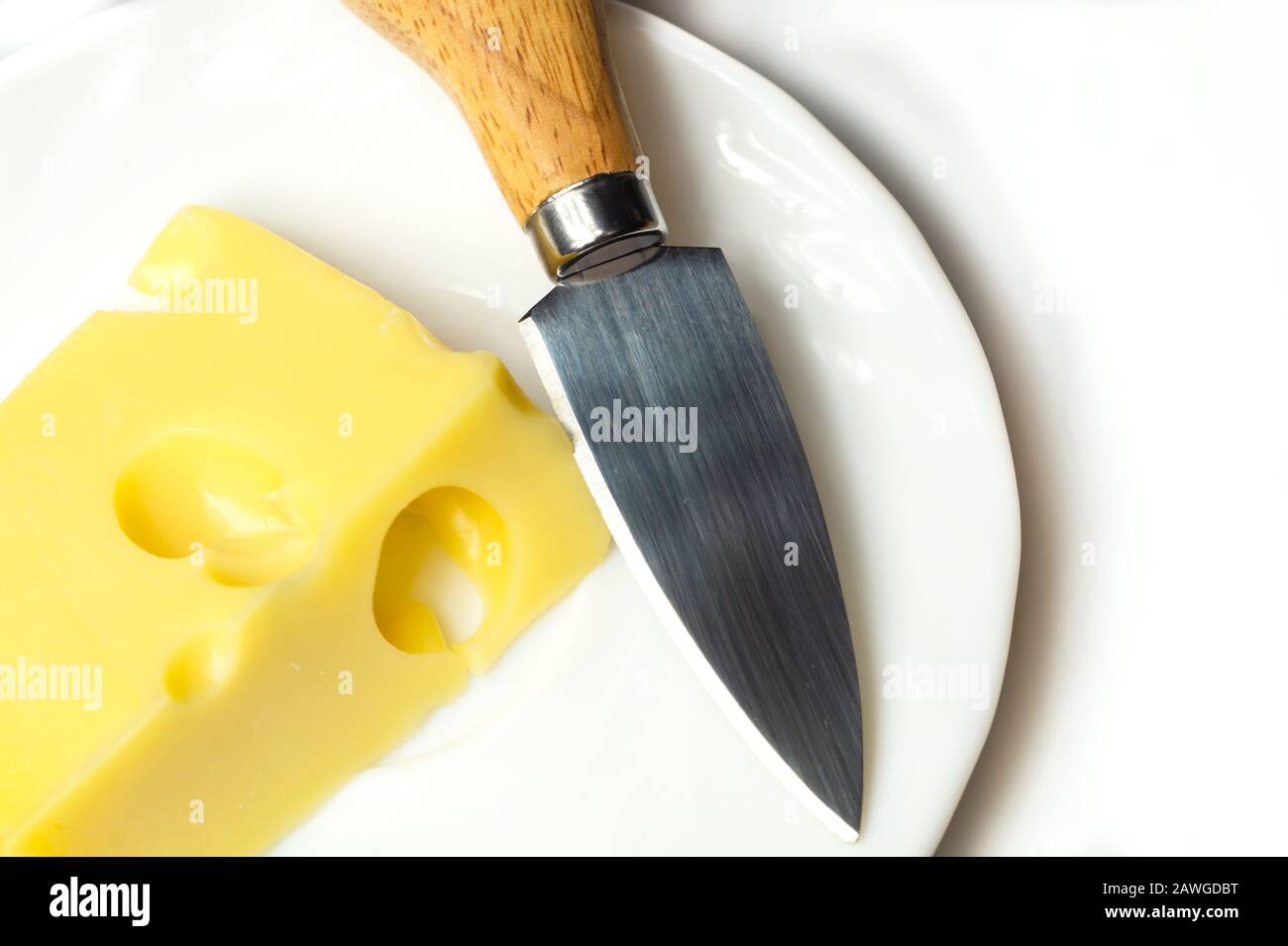 Fromage avec un couteau à fromage sur une plaque blanche. Morceau de fromage avec trous Banque D'Images