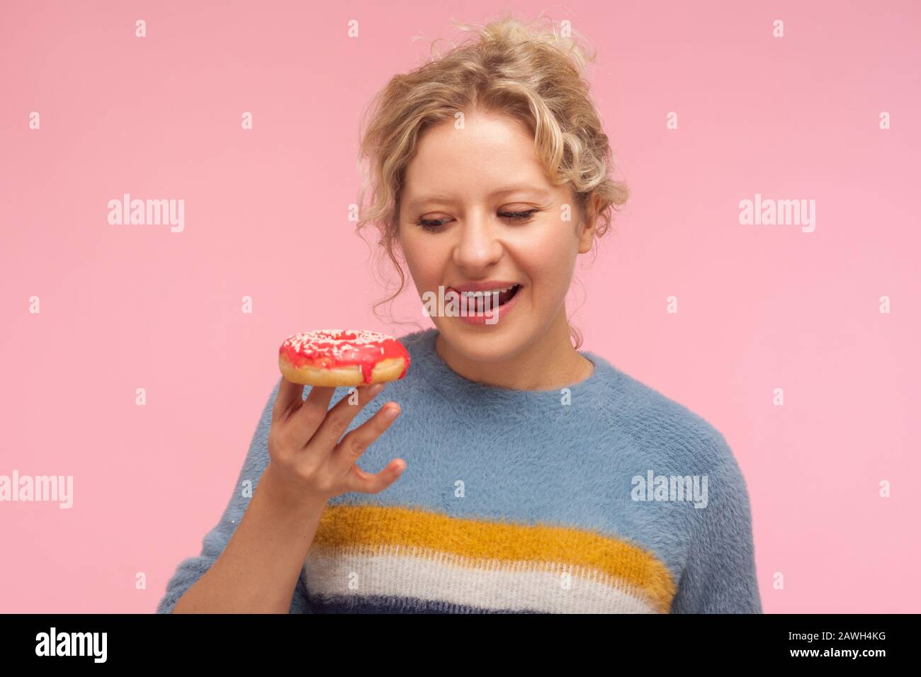 Délicieux dessert. Portrait d'une femme avec des cheveux courts et frisés dans le chandail tenant donut, regardant avec le désir de donner et de lécher ses lèvres, veut manger sw Banque D'Images