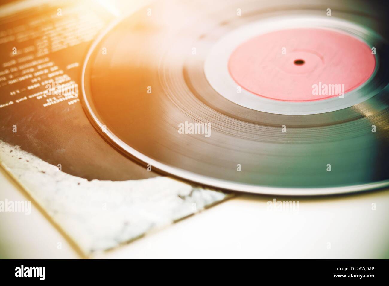 Un disque vinyle noir musical vintage se trouve sur la couverture papier d'un album de musique, éclairé par la lumière du soleil. Banque D'Images