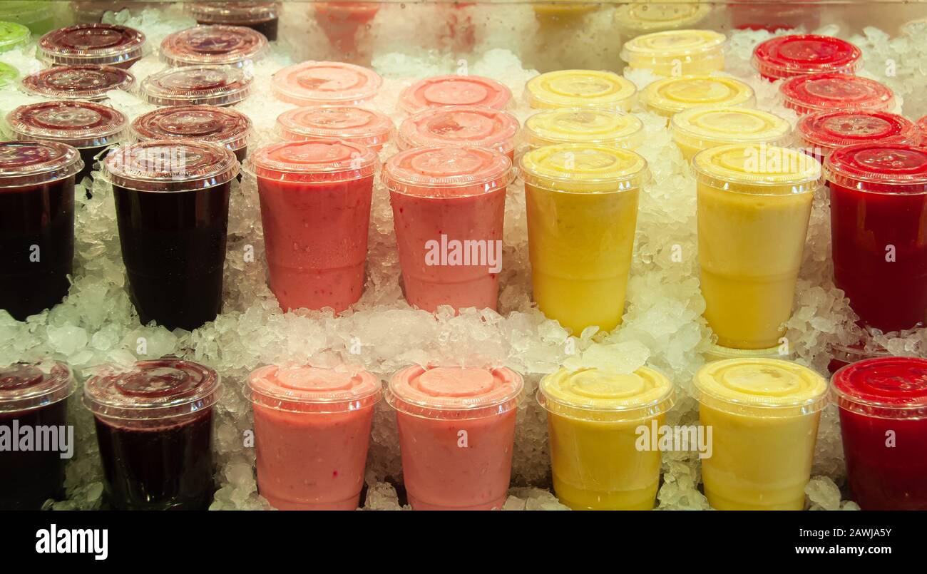 Boissons rafraîchissantes froides aux fruits, aux saveurs et aux couleurs variées, conservées dans des tasses en plastique transparent, placées en glaçons. Série de 3. Banque D'Images