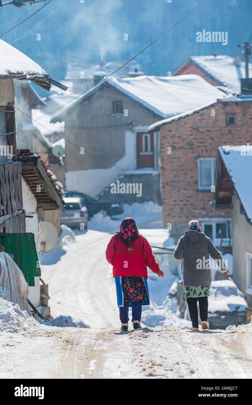 Village de Grachevo, montagnes de Rhodope, Bulgarie - 02.08.2020: La vieille femme marche sur la route enneigée en hiver dans le village de haute montagne Grachevo dans le mont Rhodopes Banque D'Images
