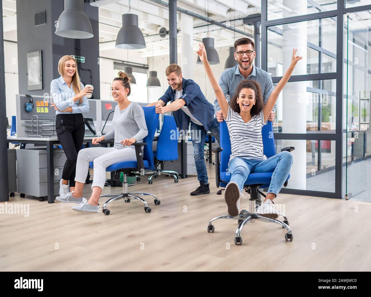 Les jeunes gens d'affaires gaie habillés en vêtements décontractés s'amusent sur des chaises d'aviron dans un bureau moderne. Heureuse équipe concept. Banque D'Images
