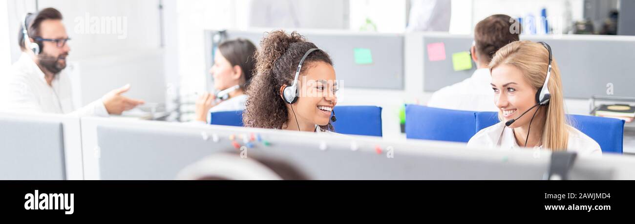 Travailleur de centre d'appel, accompagnée par son équipe. Smiling customer support au travail de l'opérateur. Jeune employé de travailler avec un casque. Banque D'Images