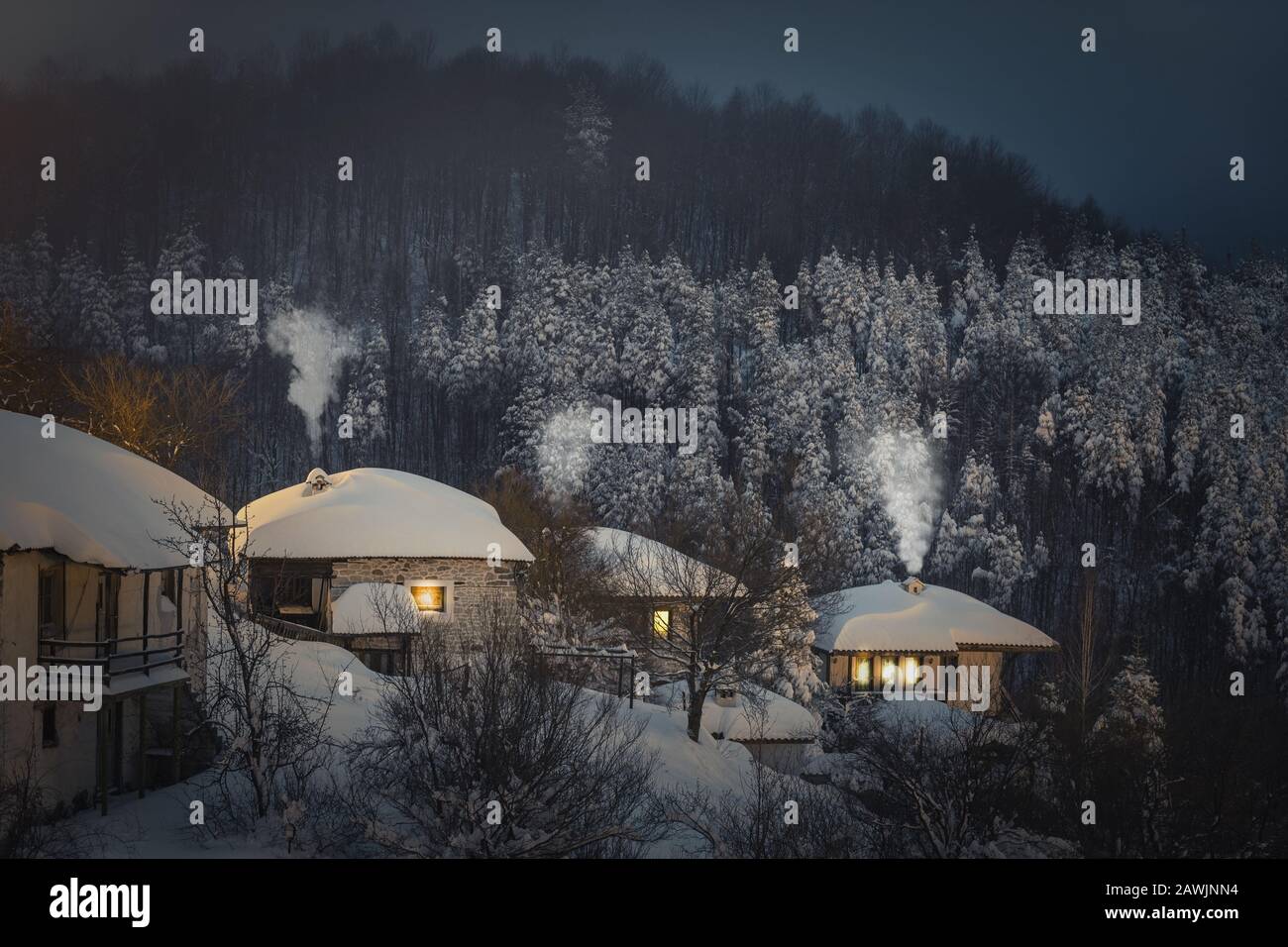 Paysage de nuit. Hiver dans la montagne de Rhodope, Bulgarie, village de Vrata. Lumière dans les fenêtres de maisons en bois. Banque D'Images