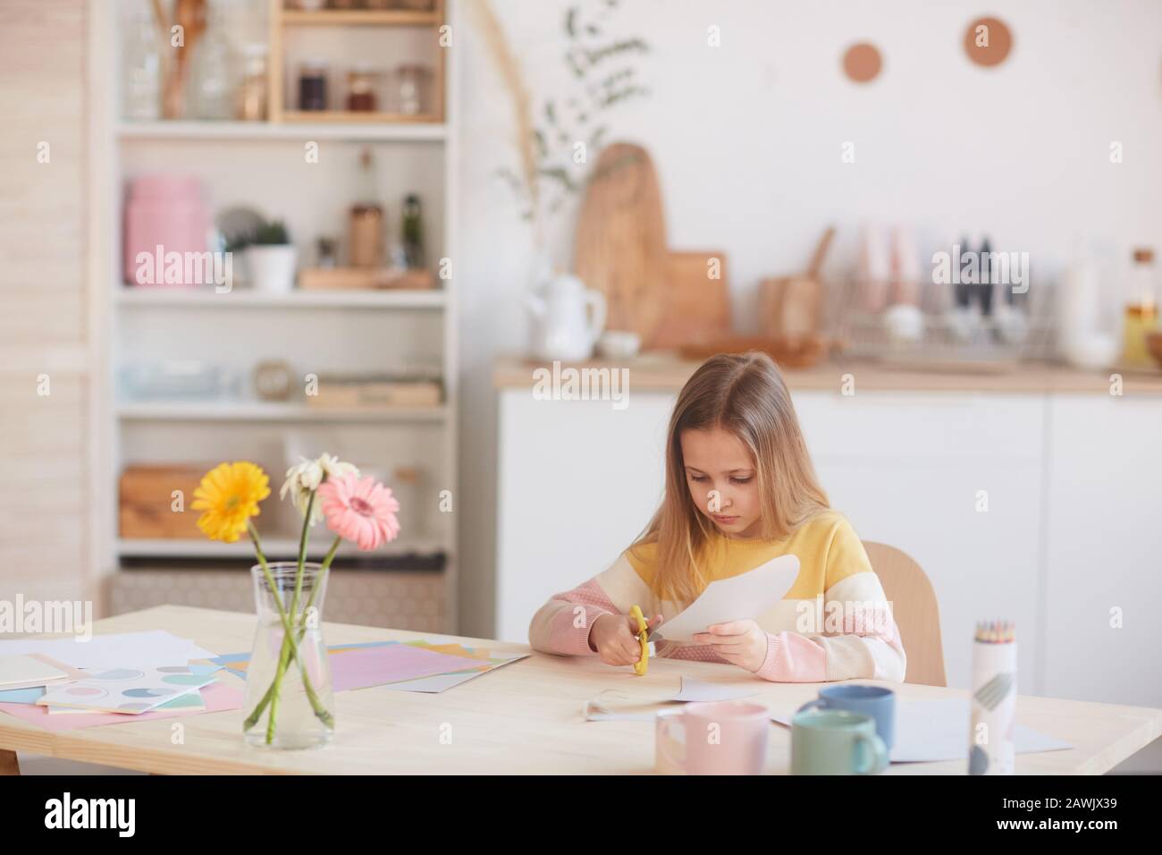 Portrait grand angle de jolie fille coupant la carte de vacances faite à la main pour La fête Des Mères ou la Saint Valentin en étant assis à la table avec des fleurs, espace de copie Banque D'Images