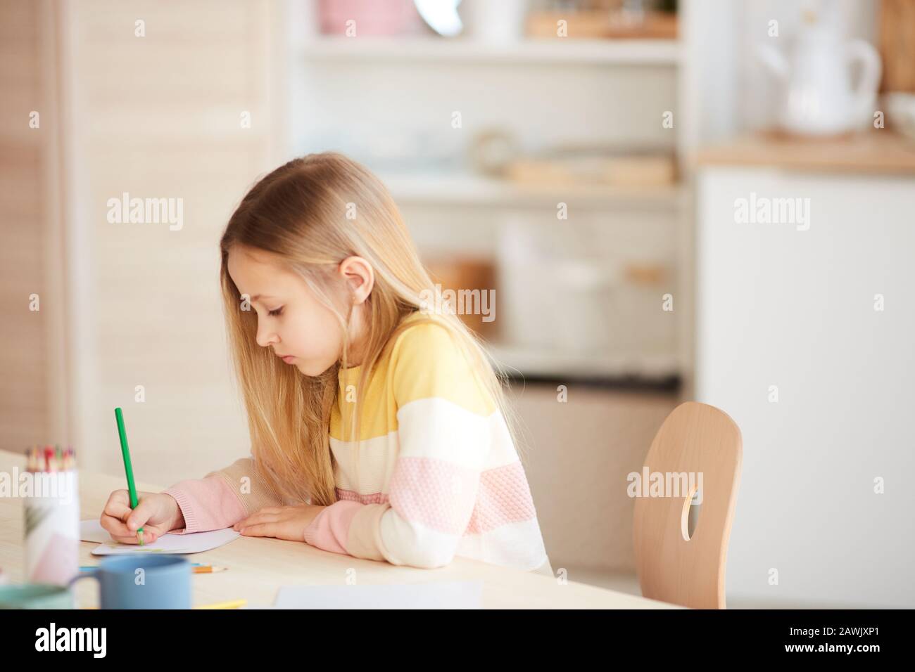 Vue latérale portrait de petite fille mignon dessin des images ou faire des devoirs tout en assis à la table dans l'intérieur de la maison, espace de copie Banque D'Images
