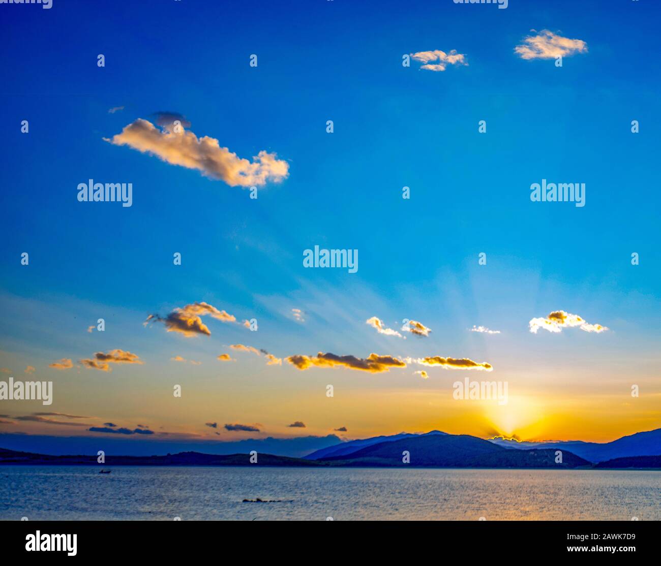 Coucher de soleil spectaculaire sur la mer derrière les montagnes, ciel bleu, lumière jaune et nuages moelleux. Banque D'Images