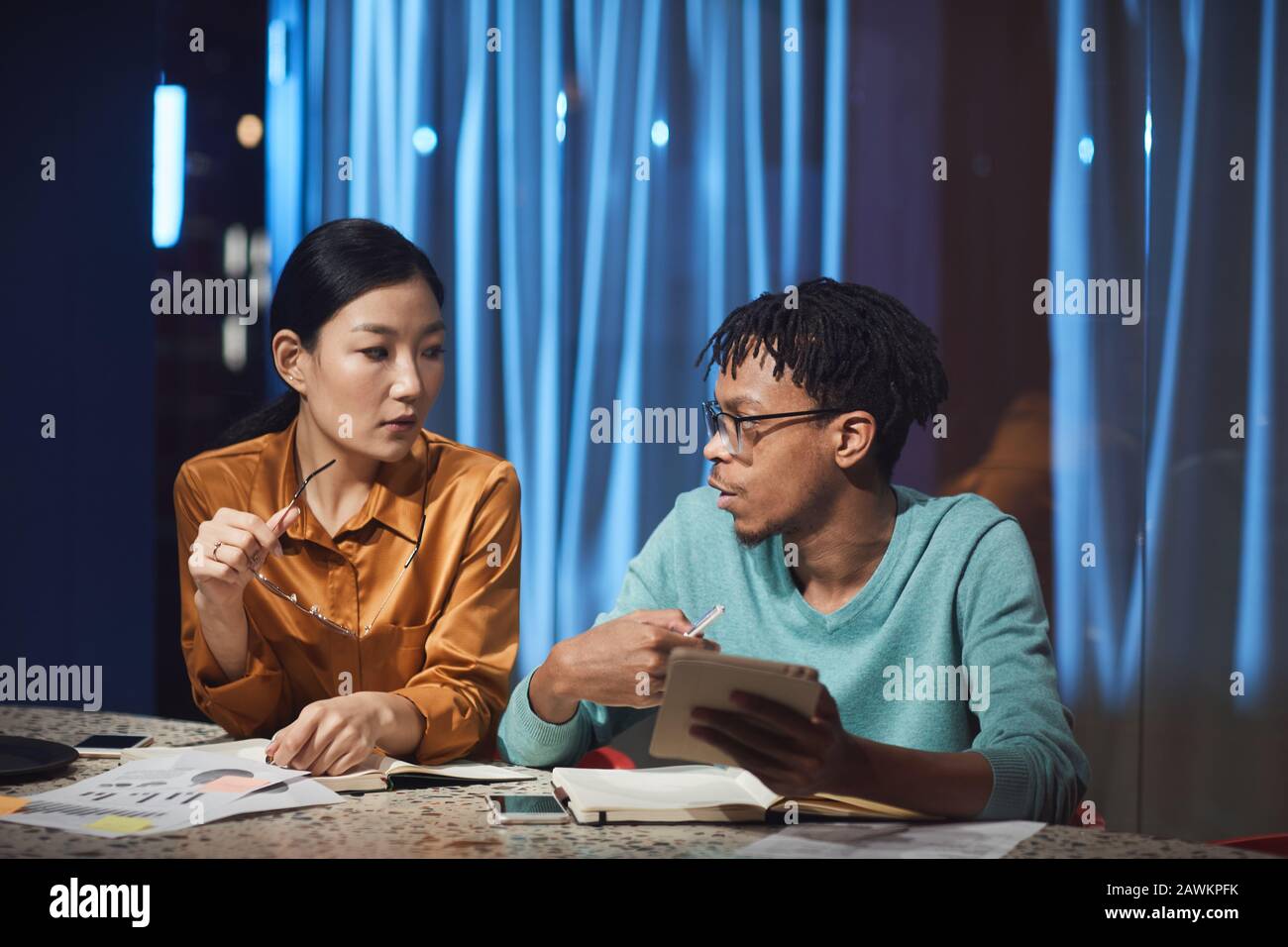 Portrait de deux personnes d'affaires ethniques discutant du projet tout en travaillant tard dans le sombre bureau, espace de copie Banque D'Images