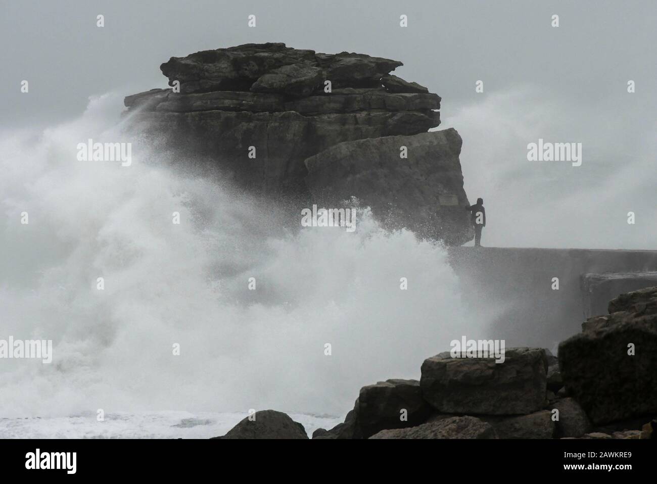 Portland Bill, Dorset, Royaume-Uni. 9 février 2020. Météo britannique. Un amateur de sensations fortes risque sa vie en marchant sur Pulpit Rock à Portland Bill à Dorset et risque d'être balayé dans la mer comme d'énormes vagues de la tempête Ciara crash contre le pilier calcaire. Crédit Photo : Graham Hunt/Alay Live News Banque D'Images