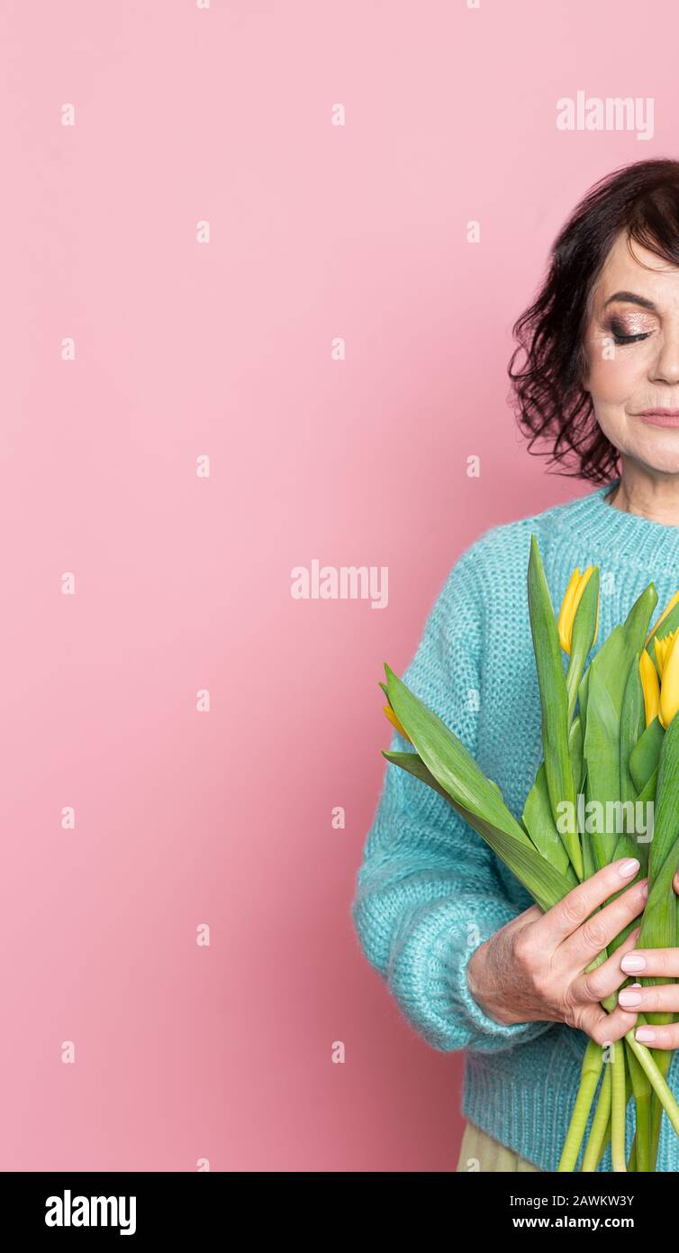 Belle vieille femme avec maquillage professionnel fumé et tenue de coiffure fleurs de tulipes sur fond rose Banque D'Images