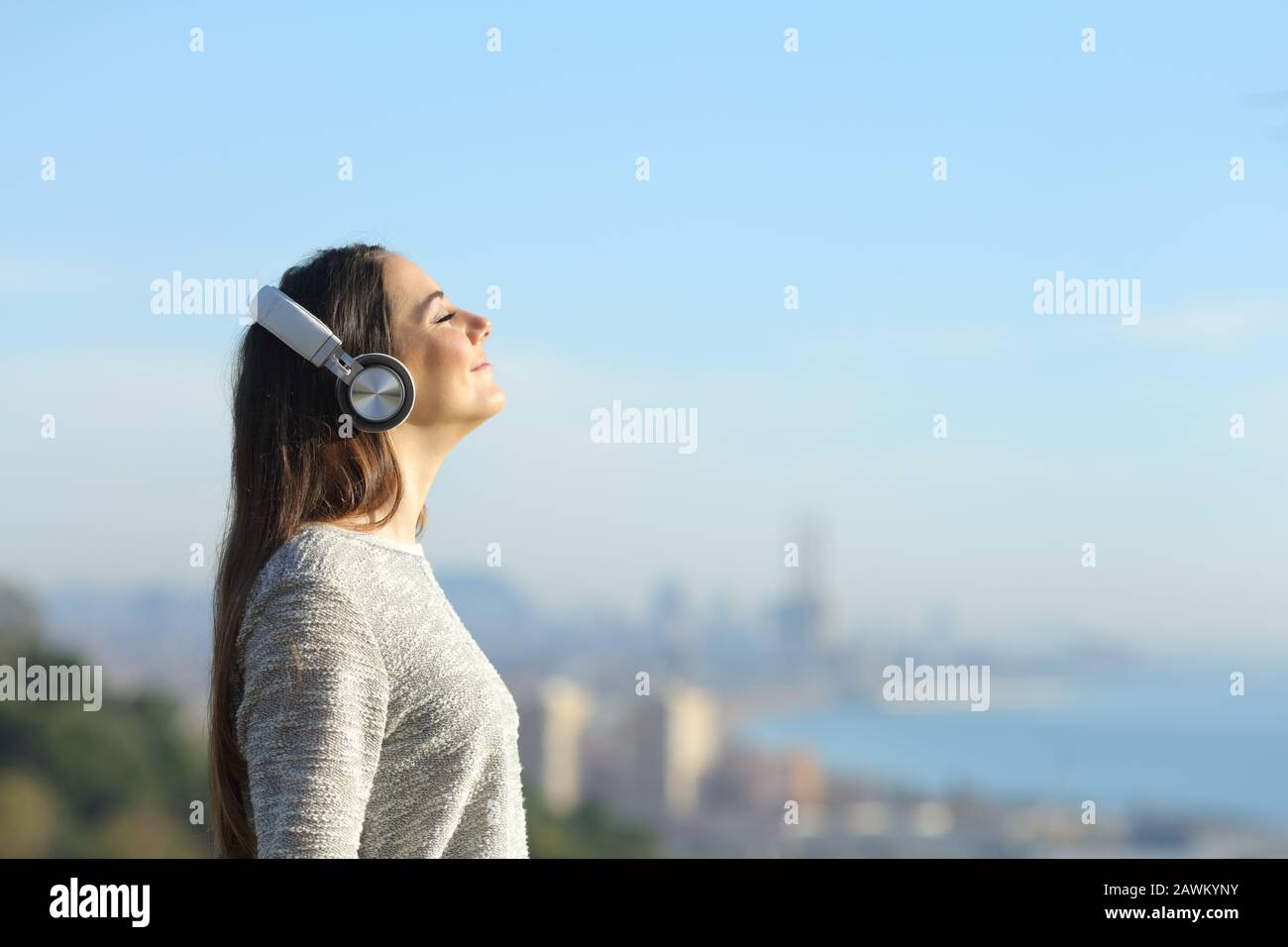 Profil d'une fille méditant écoutant de la musique respirer de l'air frais debout à l'extérieur avec une ville côtière en arrière-plan Banque D'Images