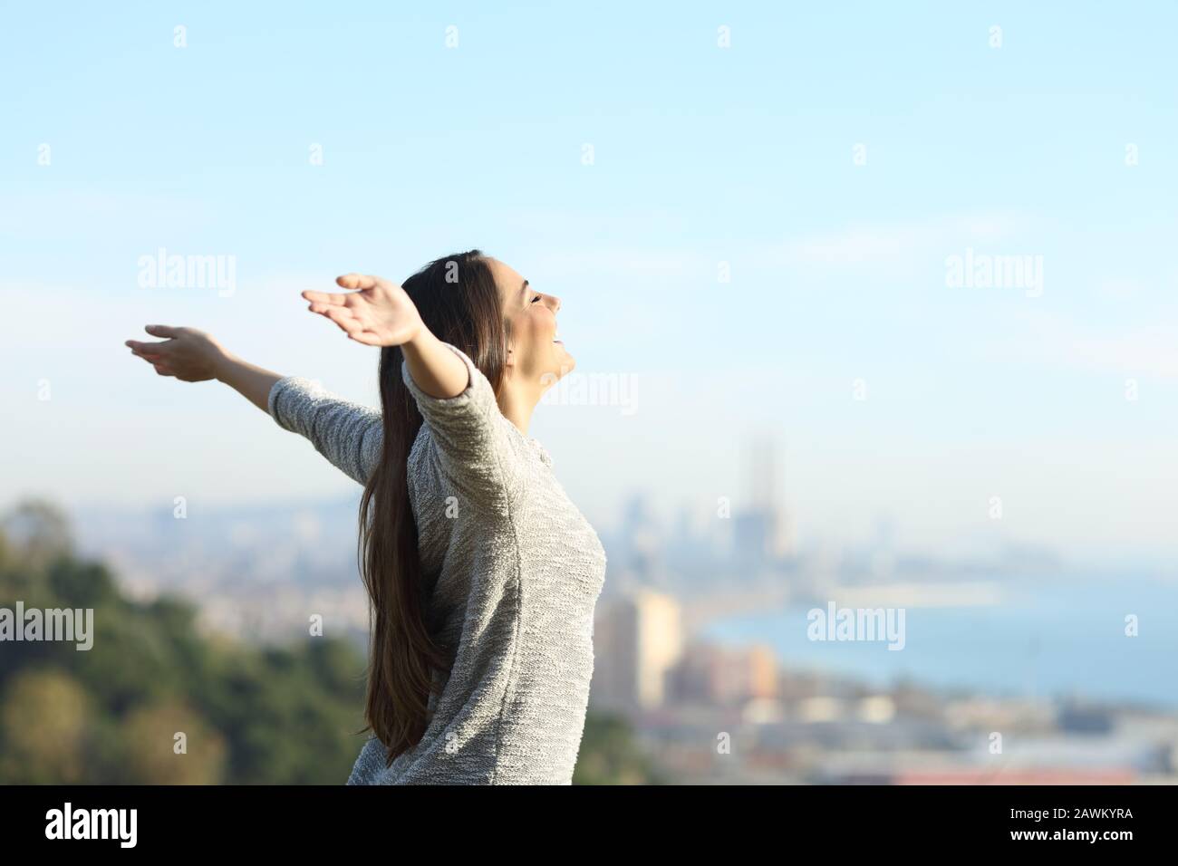 Vue latérale portrait d'une heureuse femme qui étire les bras respirer l'air frais à l'extérieur avec une ville côtière dans l'arrière-plan Banque D'Images