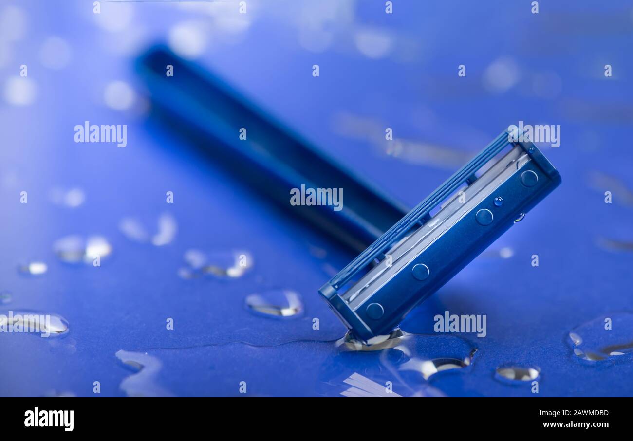 Vue macro de la lame de sécurité du rasoir sur fond de gouttes d'eau. Rasez la lame de rasage de près sur une surface humide bleue Banque D'Images