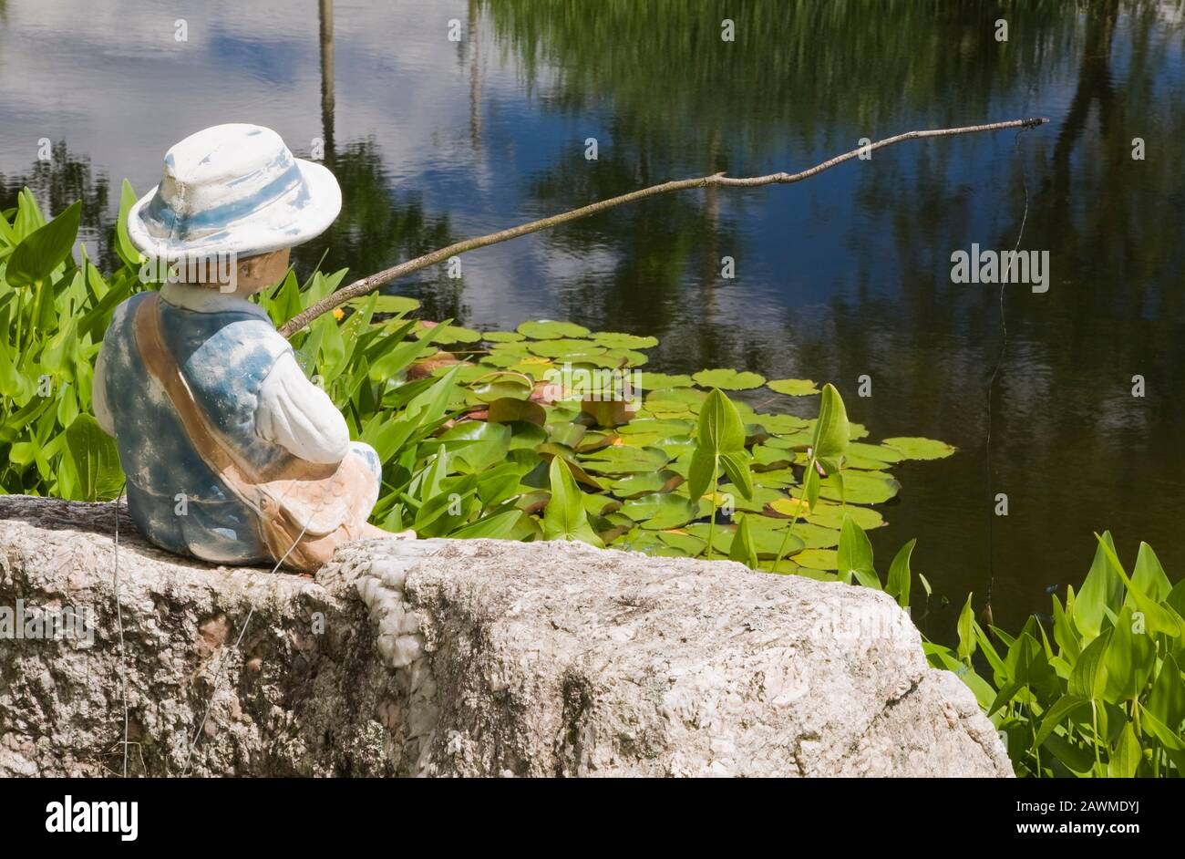 Jeune garçon en bleu Jean pêche sculpture sur l'étang avec Cordata de Pondeteria - Weed de brochet et Nymphaea - Lies d'eau dans jardin de campagne Banque D'Images