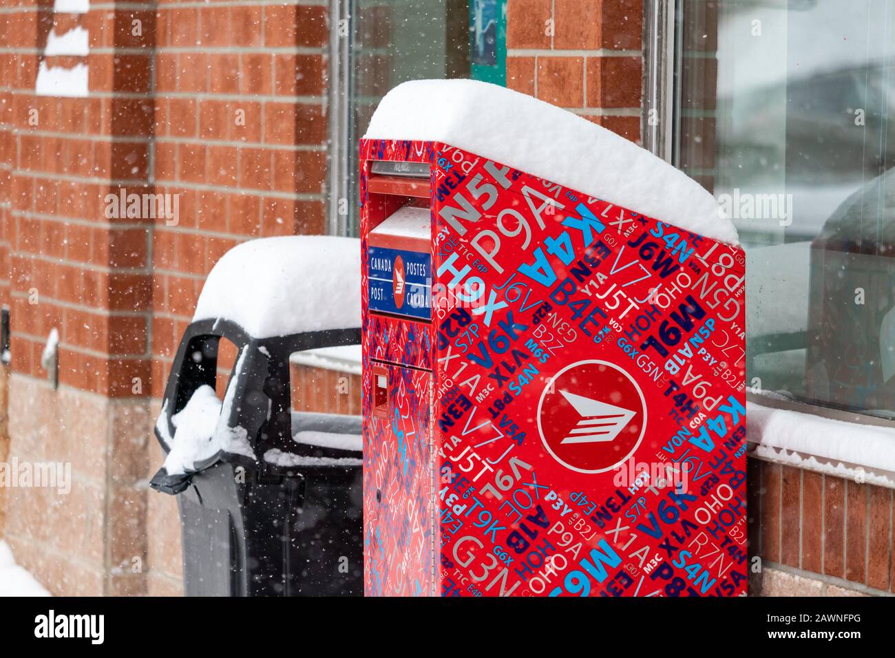 Une boîte à lettres de la rue postes Canada se trouve à l'extérieur des boutiques dans un centre commercial extérieur pendant une chute de neige en hiver, avec une couche de neige sur la boîte aux lettres. Banque D'Images