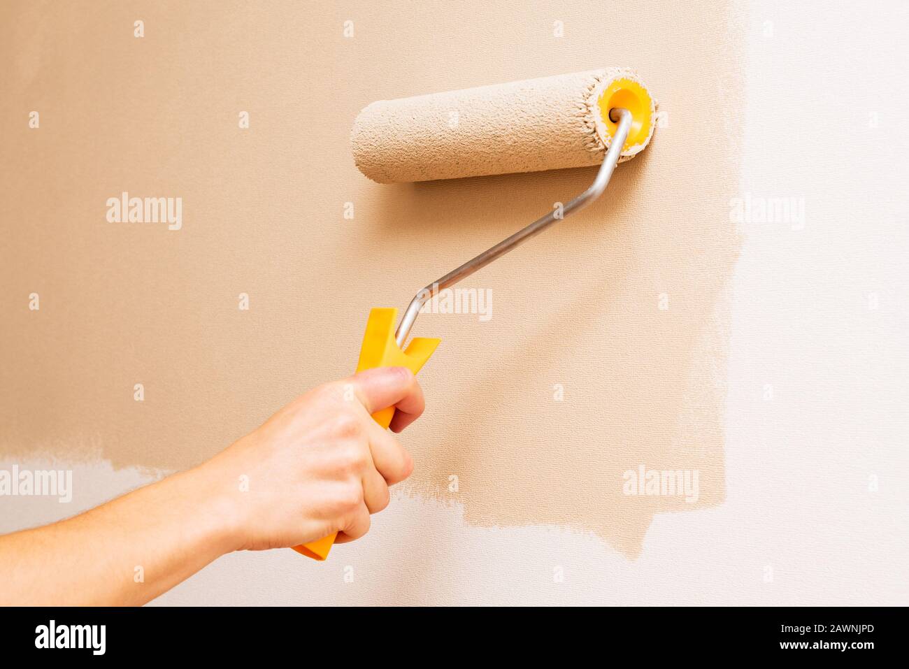 Peindre le mur avec un rouleau de peinture en beige Banque D'Images