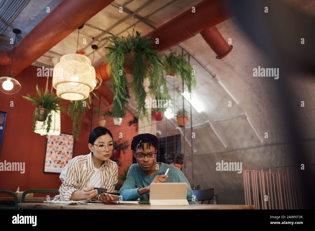 Portrait grand angle de deux étudiants contemporains travaillant ensemble sur le projet tout en étant assis à la table dans un café, espace de copie Banque D'Images