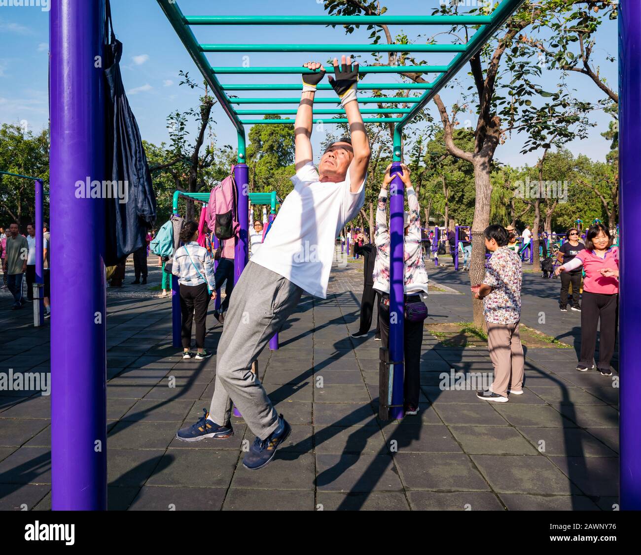 Homme chinois plus âgé exerçant dans une salle de gym extérieure se balançant sur des rails de bar, Tiantan Park, Beijing, Chine, Asie Banque D'Images