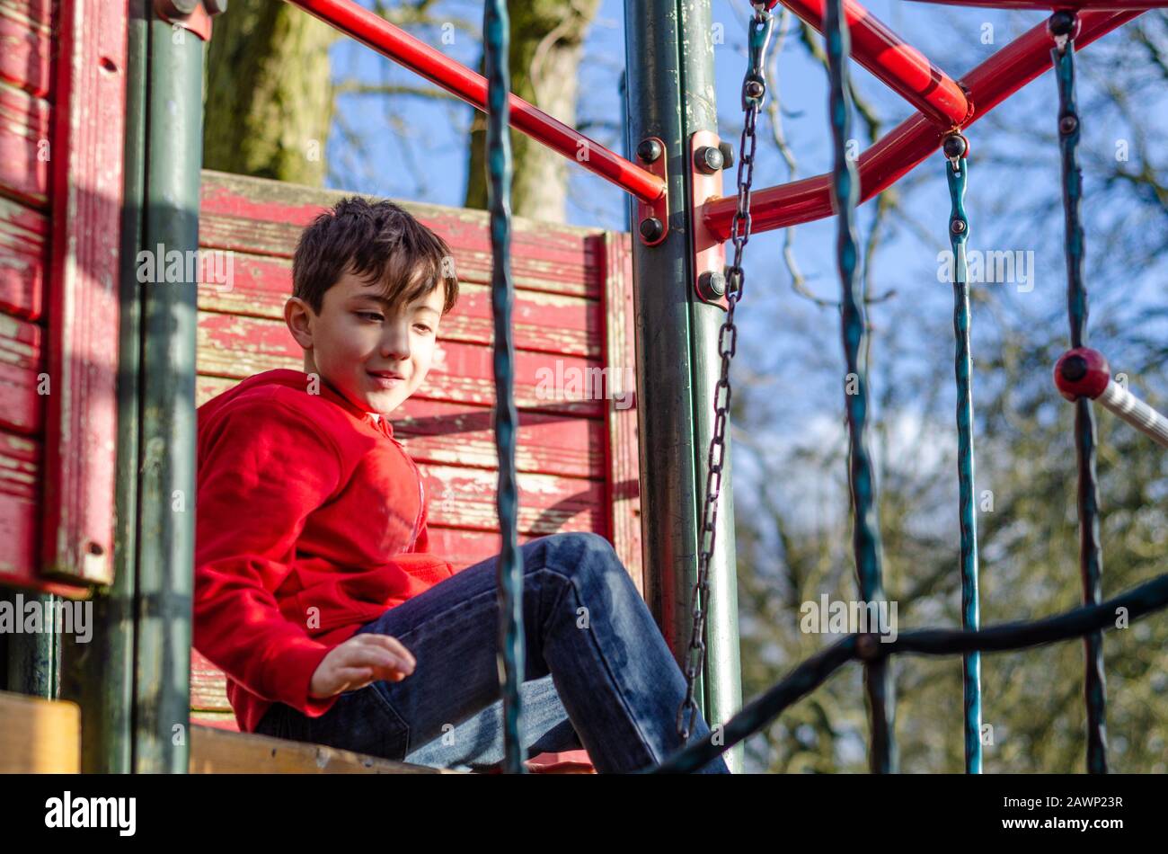 Un jeune garçon heureux de jouer sur un cadre d'escalade dans une aire de jeux pour enfants. Banque D'Images