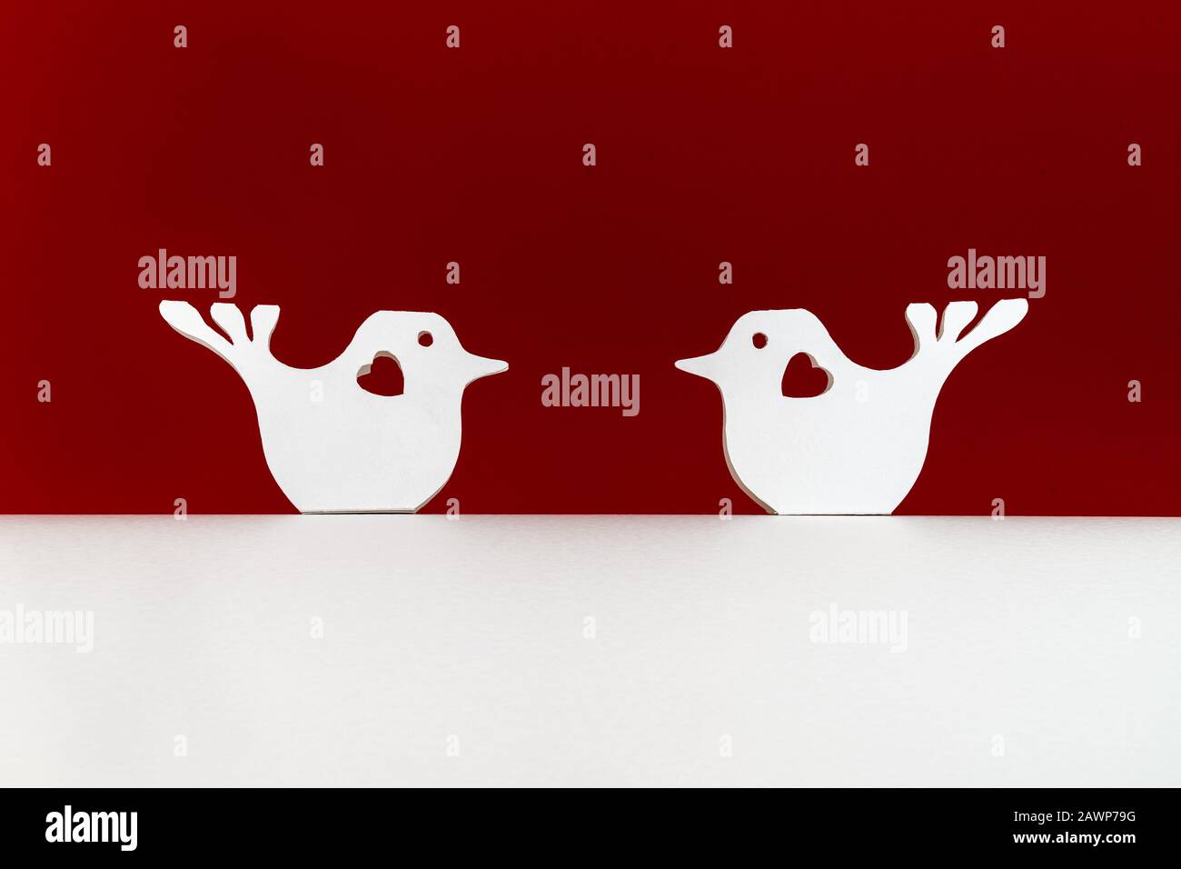 Deux oiseaux blancs coupés en papier avec des coeurs assis sur une base de carton blanc sur un fond rouge foncé. Concept de Saint Valentin. Carte de vacances avec copie spac Banque D'Images