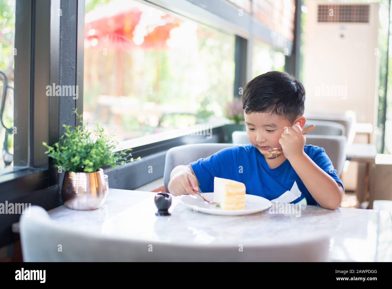 Cute little Asian boy eating cake dans une boulangerie ou un café. Banque D'Images