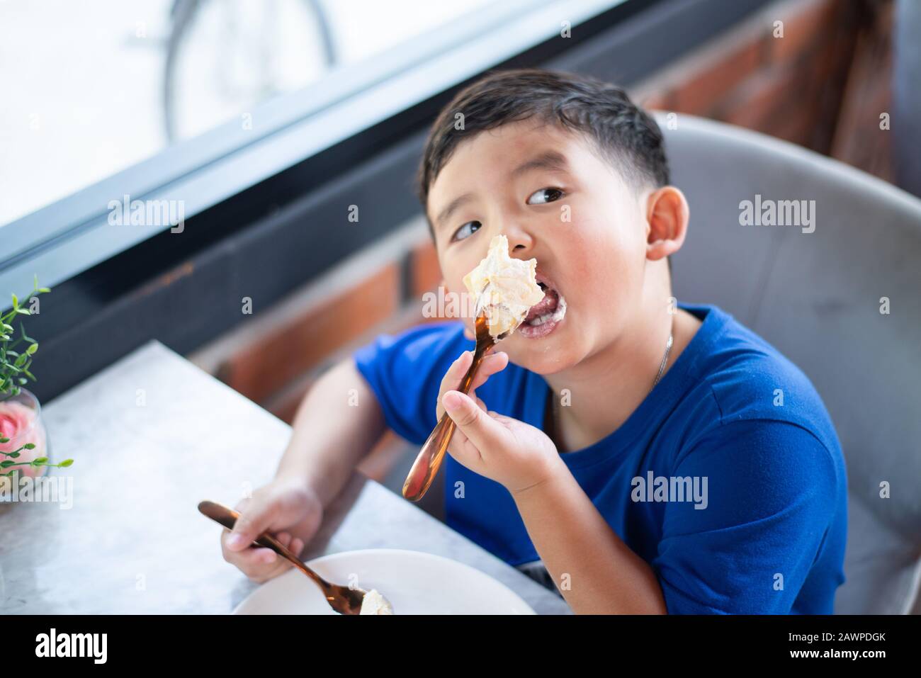 Cute little Asian boy eating cake dans une boulangerie ou un café. Banque D'Images