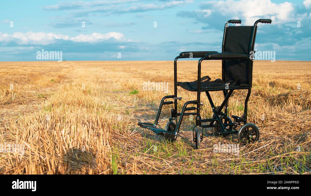 Fauteuil roulant vide dans un grand pré. Chariot pour personnes handicapées dans la nature. Équipement médical pour personne non valide. Champ de division de ligne Horizon et ciel Banque D'Images