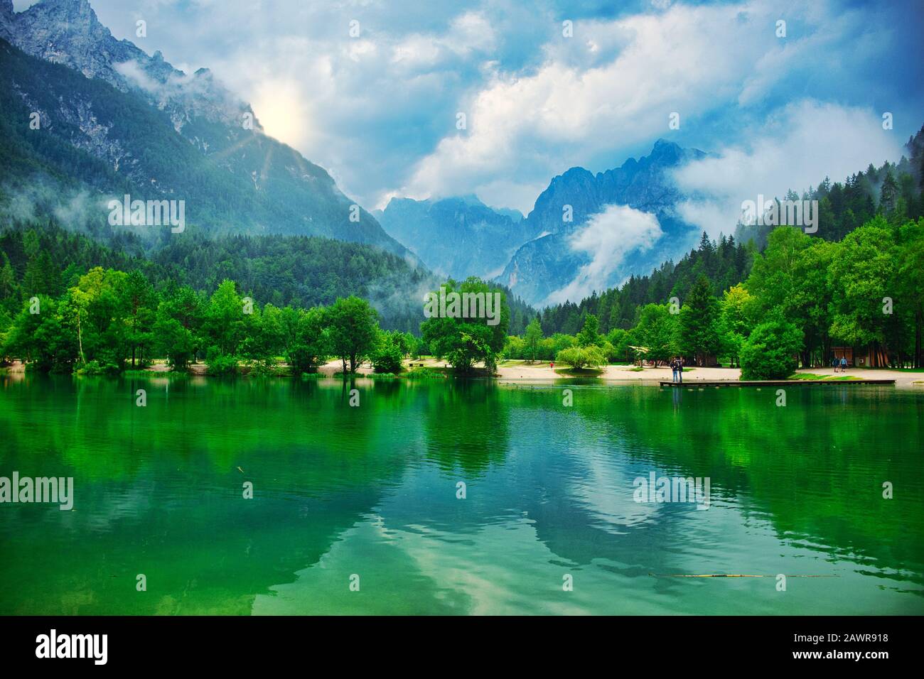 Paysage de lac de montagne, avec un écrin de pin vert luxuriant, des nuages brumeux et un coucher de soleil de derrière un pic Banque D'Images