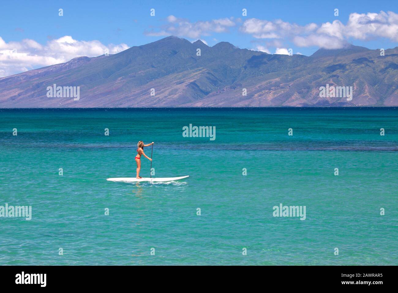 Une femme en forme et en bonne santé paddle un panneau de paddle debout à Napili Bay, Maui, Hawaï. Molokai au loin. Banque D'Images