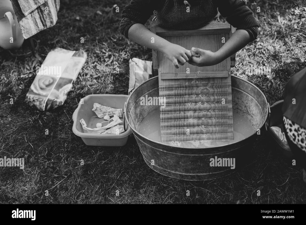 Un enfant se lave des vêtements dans une ancienne baignoire de lavage en zinc avec une planche à laver en bois Banque D'Images