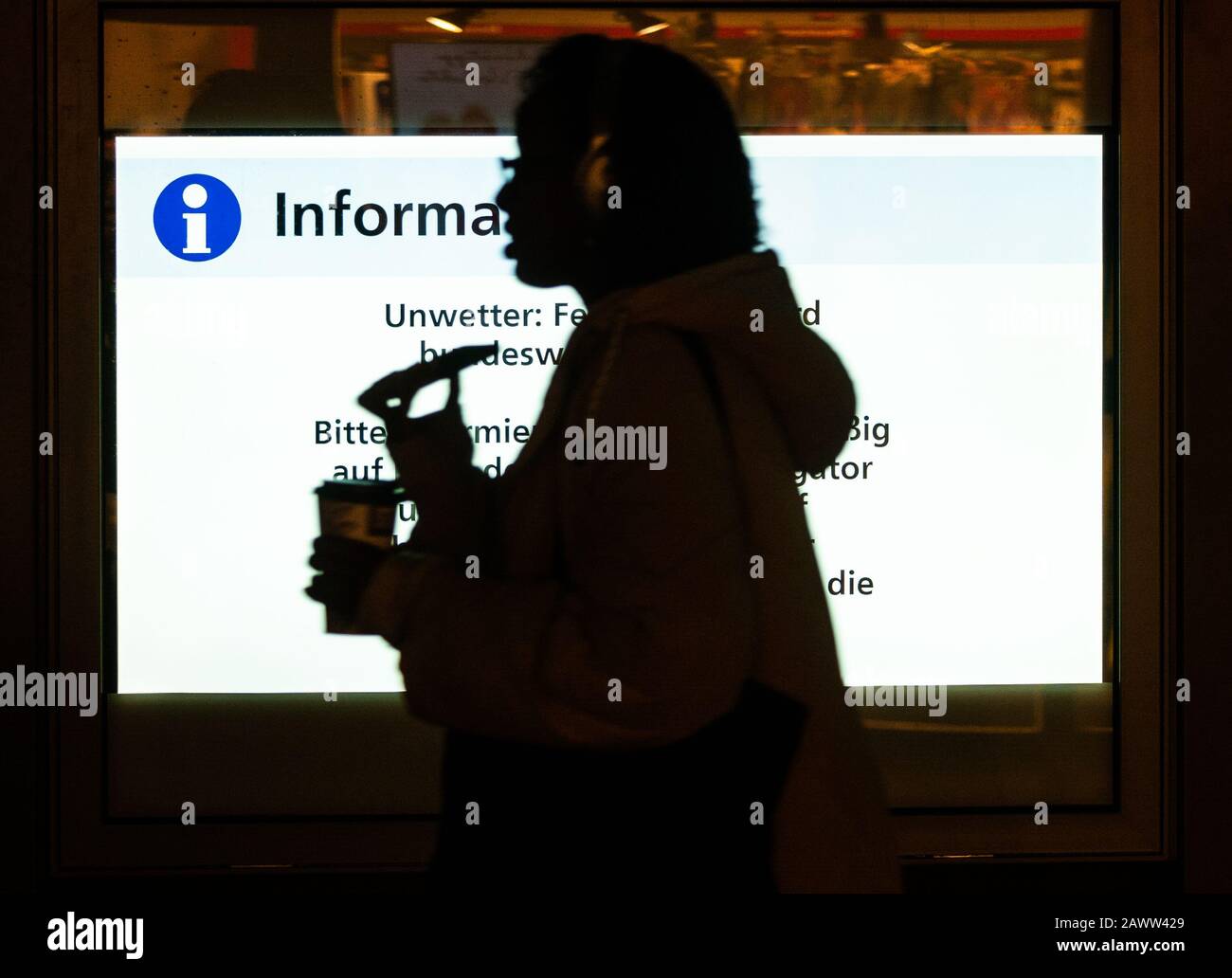 10 février 2020, Hessen, Francfort-sur-le-Main: Une femme passe devant un panneau d'information à la gare principale de Francfort avec son smartphone et une tasse de café dans la main. En raison de la tempête Sabine, il y a des défaillances et des perturbations massives dans la circulation ferroviaire à l'échelle nationale. Photo: Andreas Arnold/Dpa Banque D'Images