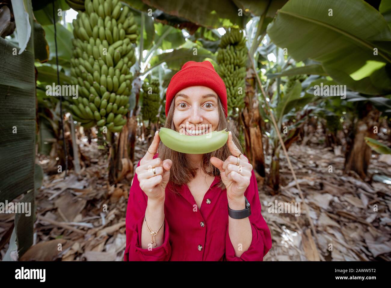 Portrait d'une jolie femme vêtue de fruits de banane à mordre rouge sur la plantation. Concept de consommation de fruits frais Banque D'Images
