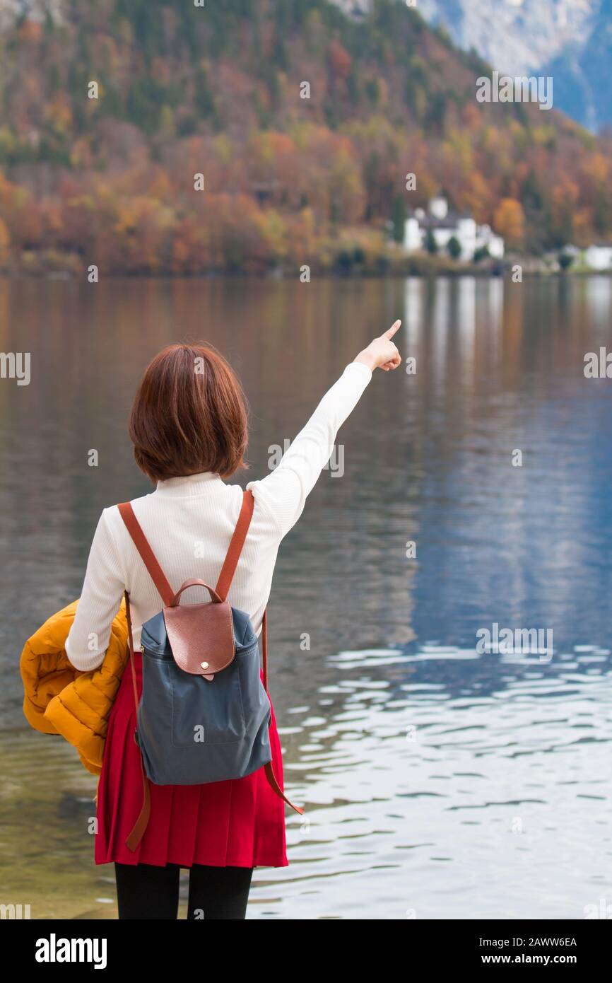 Une jeune fille de touristes asiatiques de l'arrière se tenant le doigt de pointage au lac Hallstatt Autriche en automne; liberté paisible concept de détente Banque D'Images