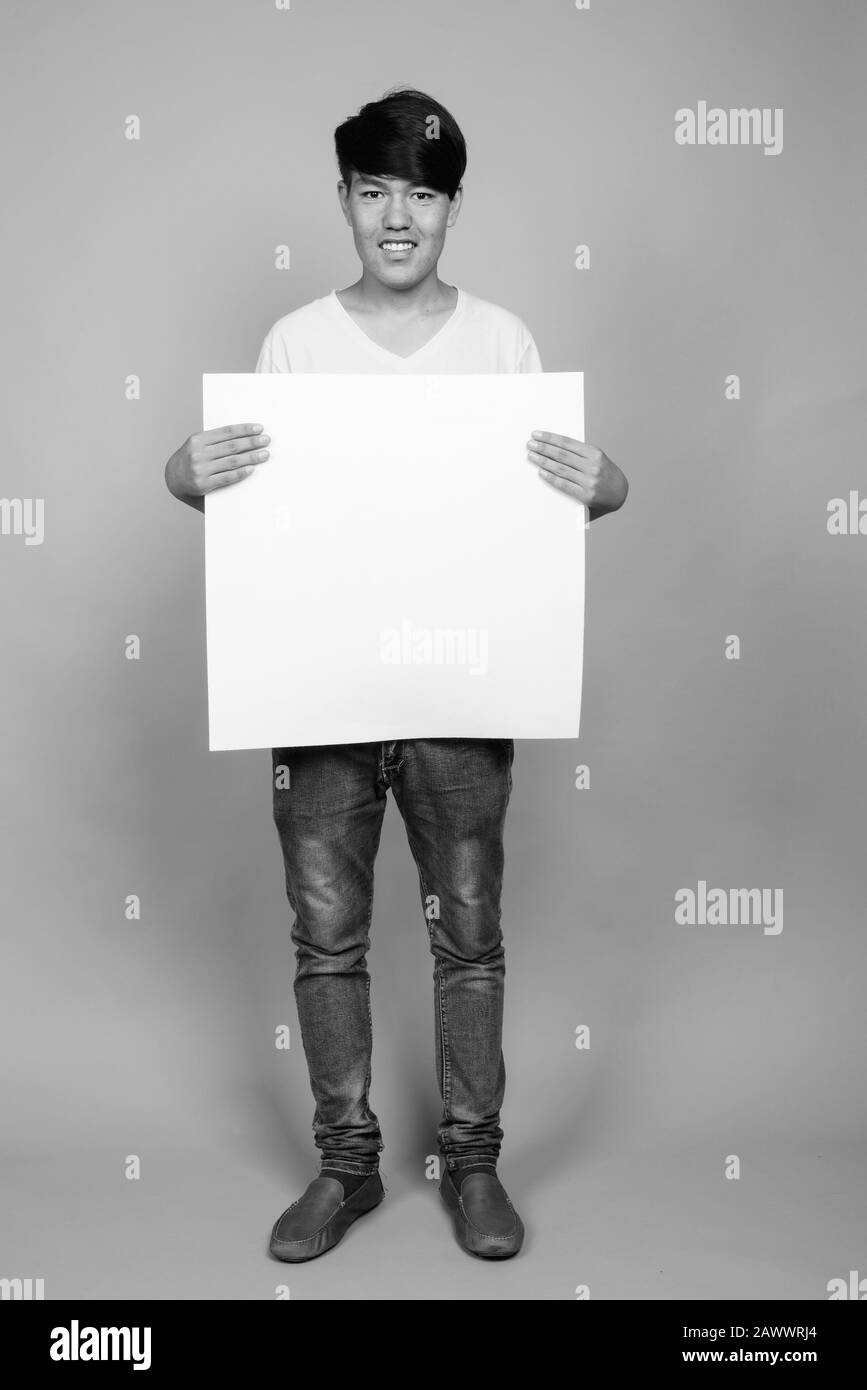 Jeune adolescent asiatique tenant un tableau blanc sur fond gris Banque D'Images