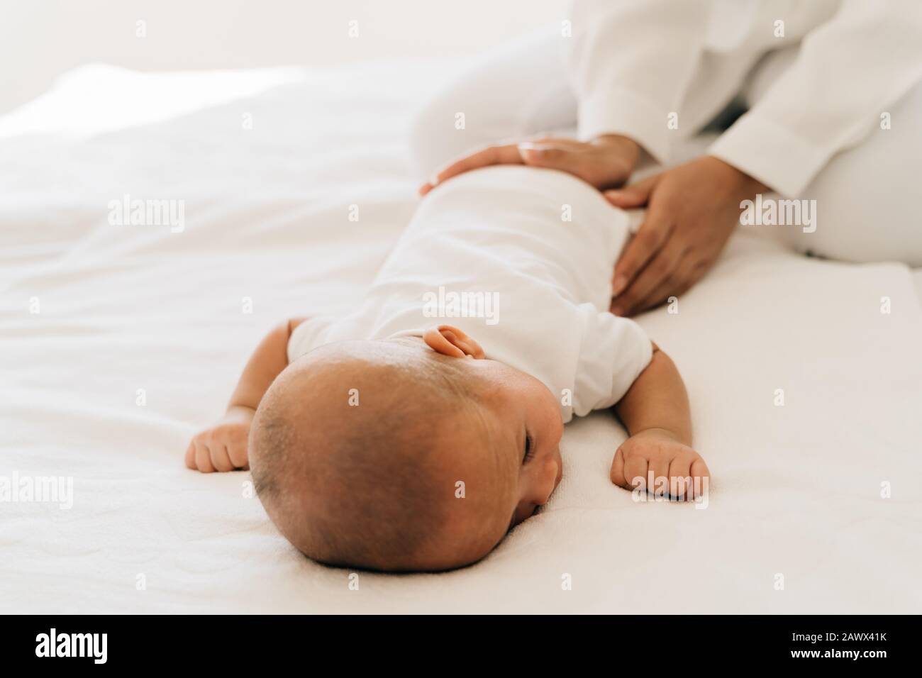 D'en haut de mère attentionnée avec la mère du nouveau-né patting bébé asiatique petit enfant allongé sur le ventre dans la chambre à la maison Banque D'Images