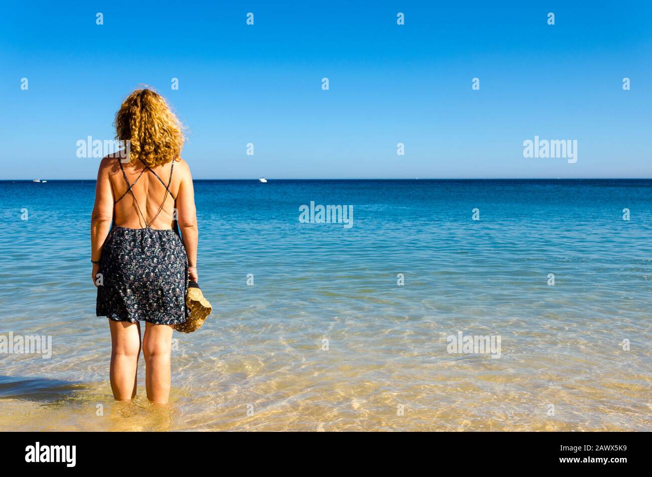 Blonde avec des cheveux frisés, en regardant la mer sur la plage de Salema, Algarve, Portugal Banque D'Images