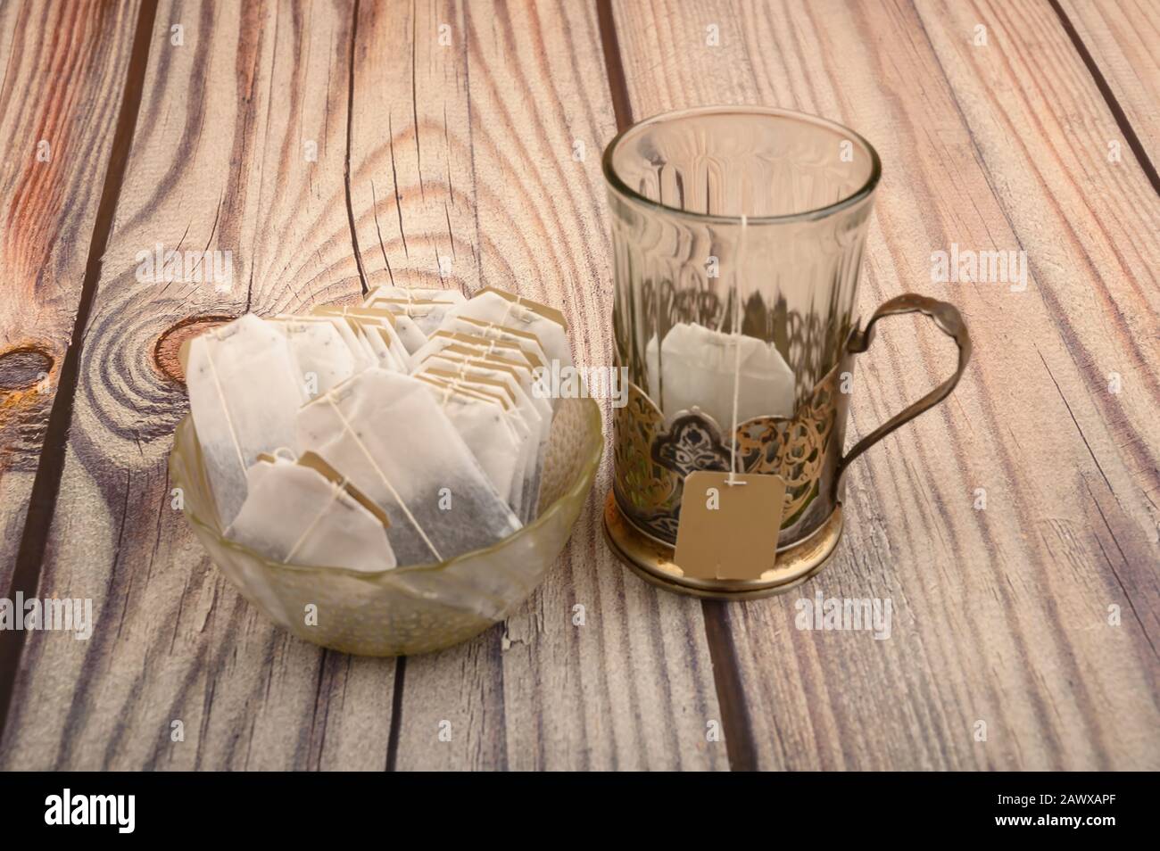 Sachets de thé dans un vase en verre et un verre à facettes vide dans un porte-gobelet vintage sur fond en bois. Gros plan Banque D'Images