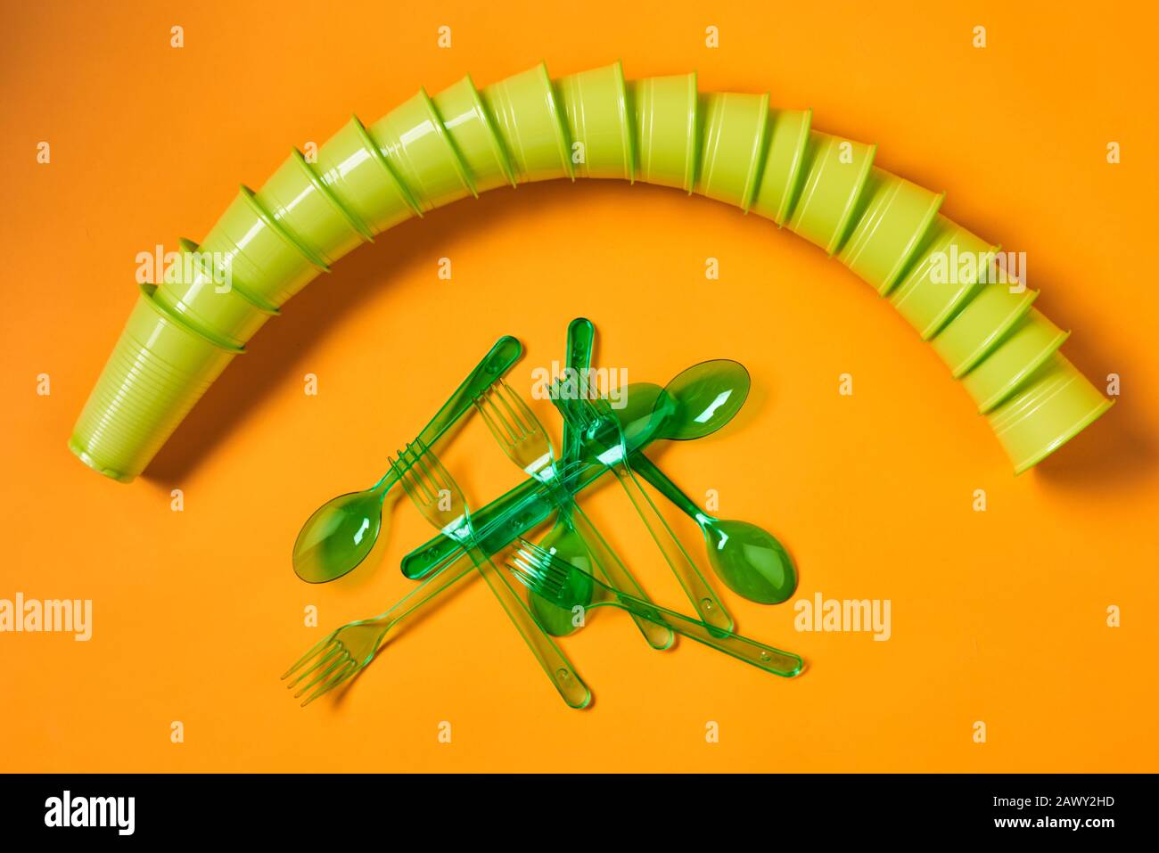 Plan horizontal plat de jeu de tasses en plastique vert jetables, cuillères et fourchettes sur fond orange vif Banque D'Images
