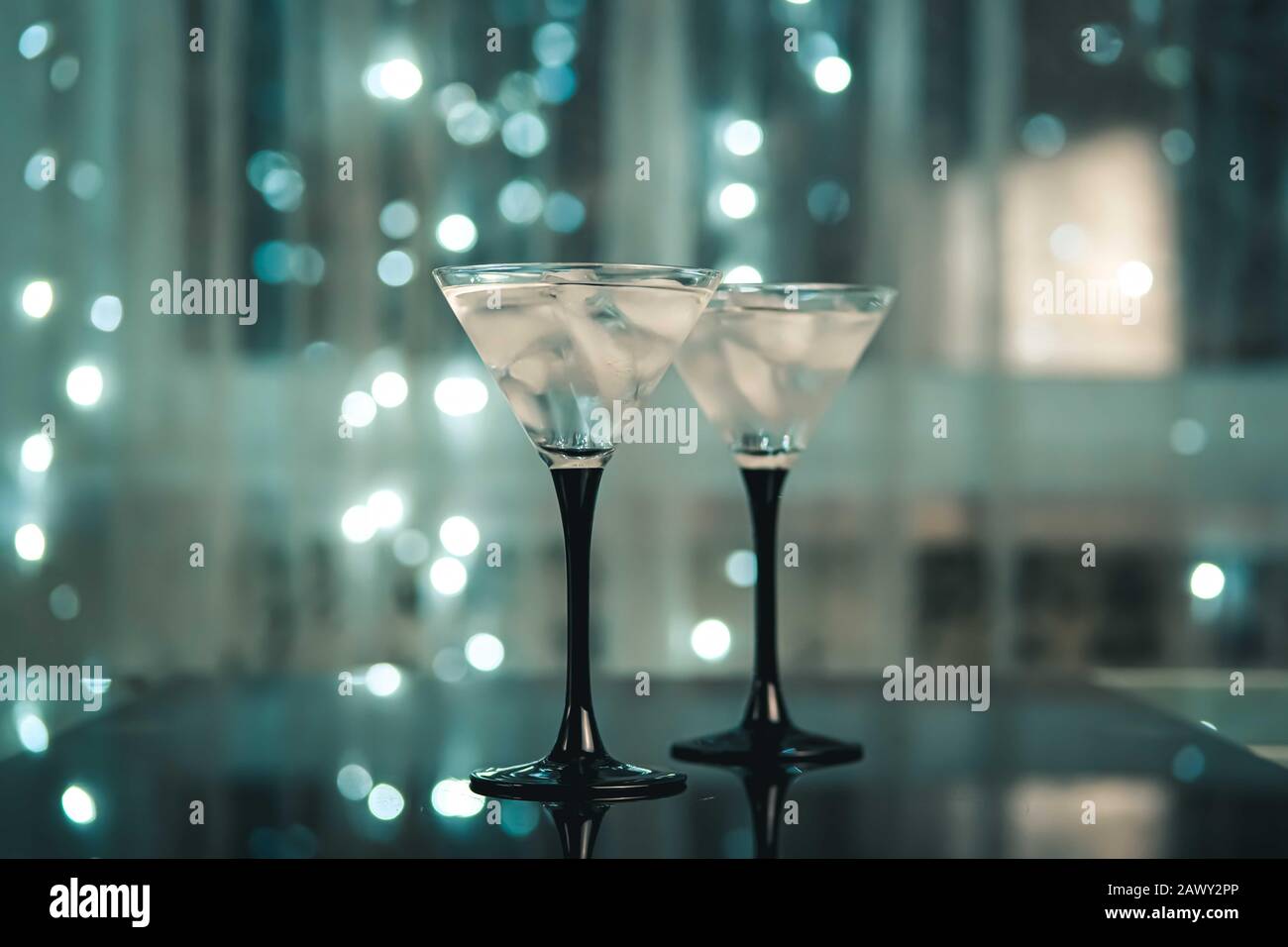 Deux verres à cocktail avec boisson martini avec glace sur fond noir tendance avec lumières bokeh. Concept de date du soir ou de la nuit. Banque D'Images