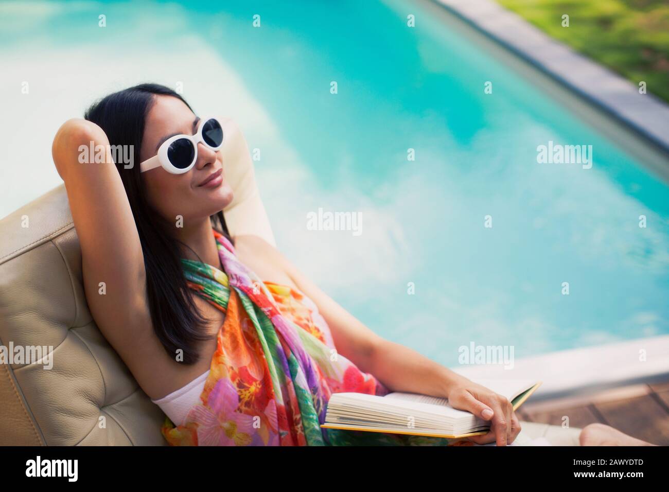 Une femme sereine et relaxante, livre de lecture au bord de la piscine en été Banque D'Images