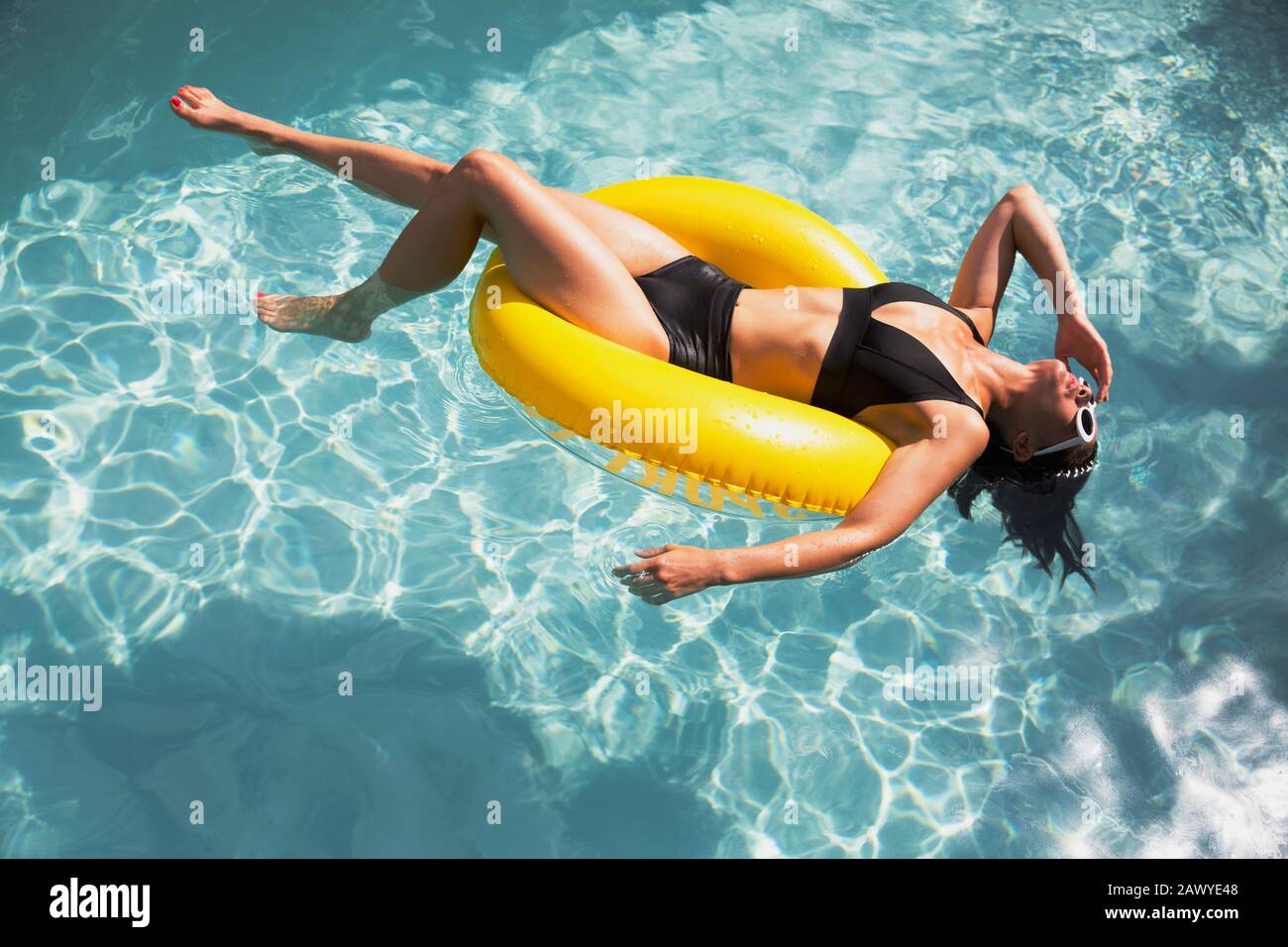 Femme sensuelle au bikini flottant sur l'anneau gonflable jaune dans la piscine ensoleillée Banque D'Images