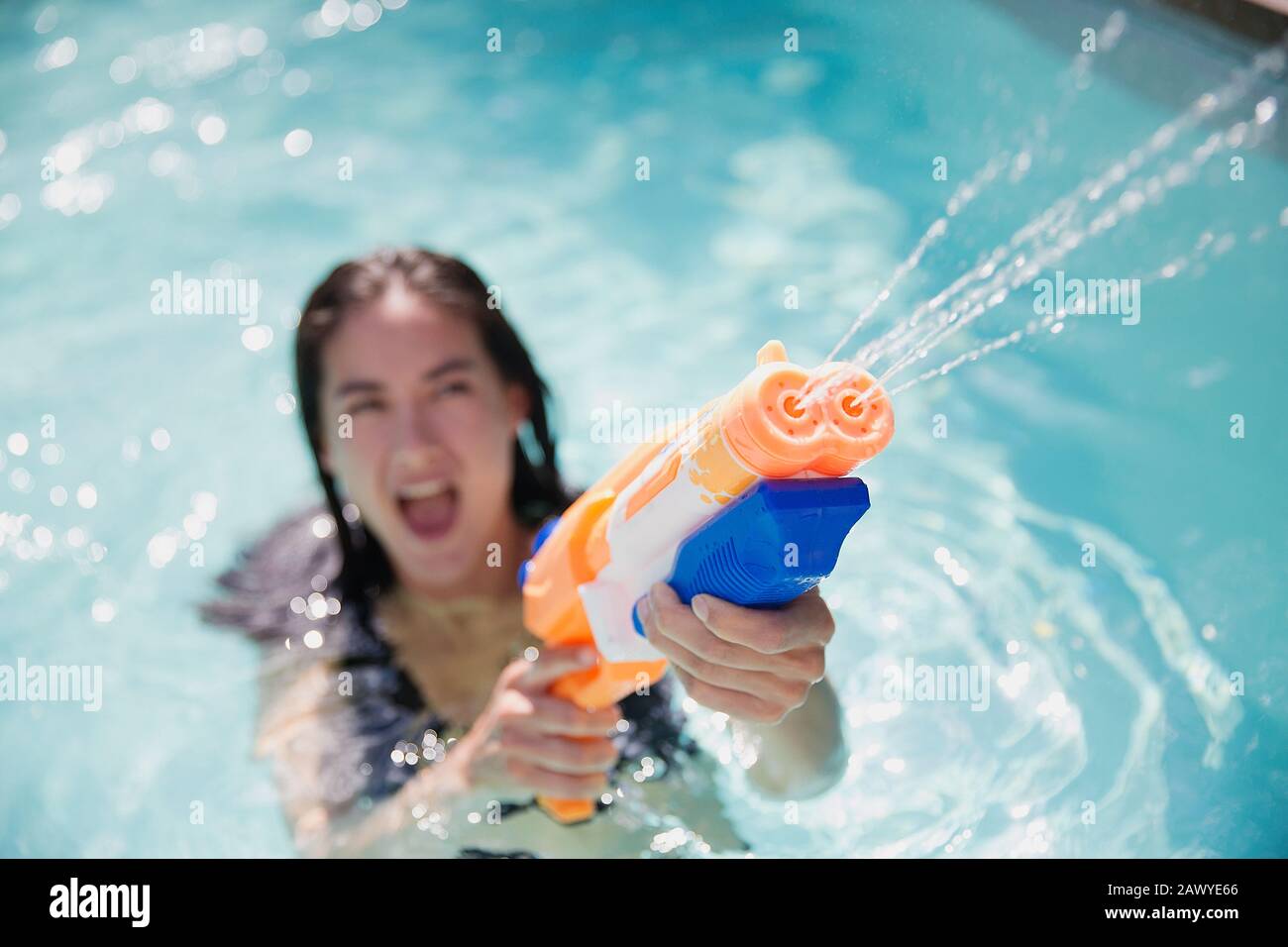 Une femme espiègle à l'aide d'un pistolet dans la piscine d'été ensoleillée Banque D'Images