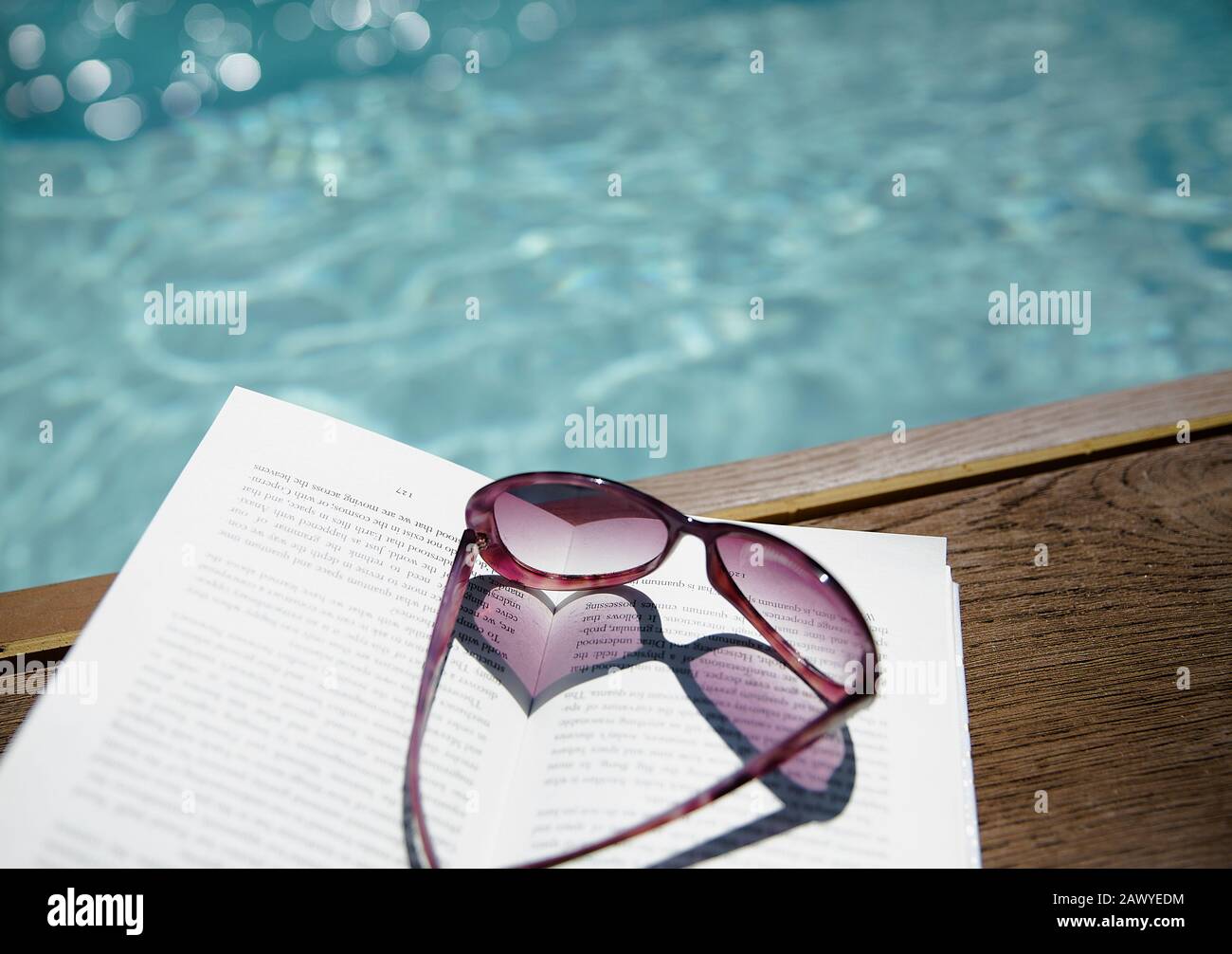 Lunettes de soleil en forme de coeur sur le livre au bord de la piscine ensoleillée Banque D'Images